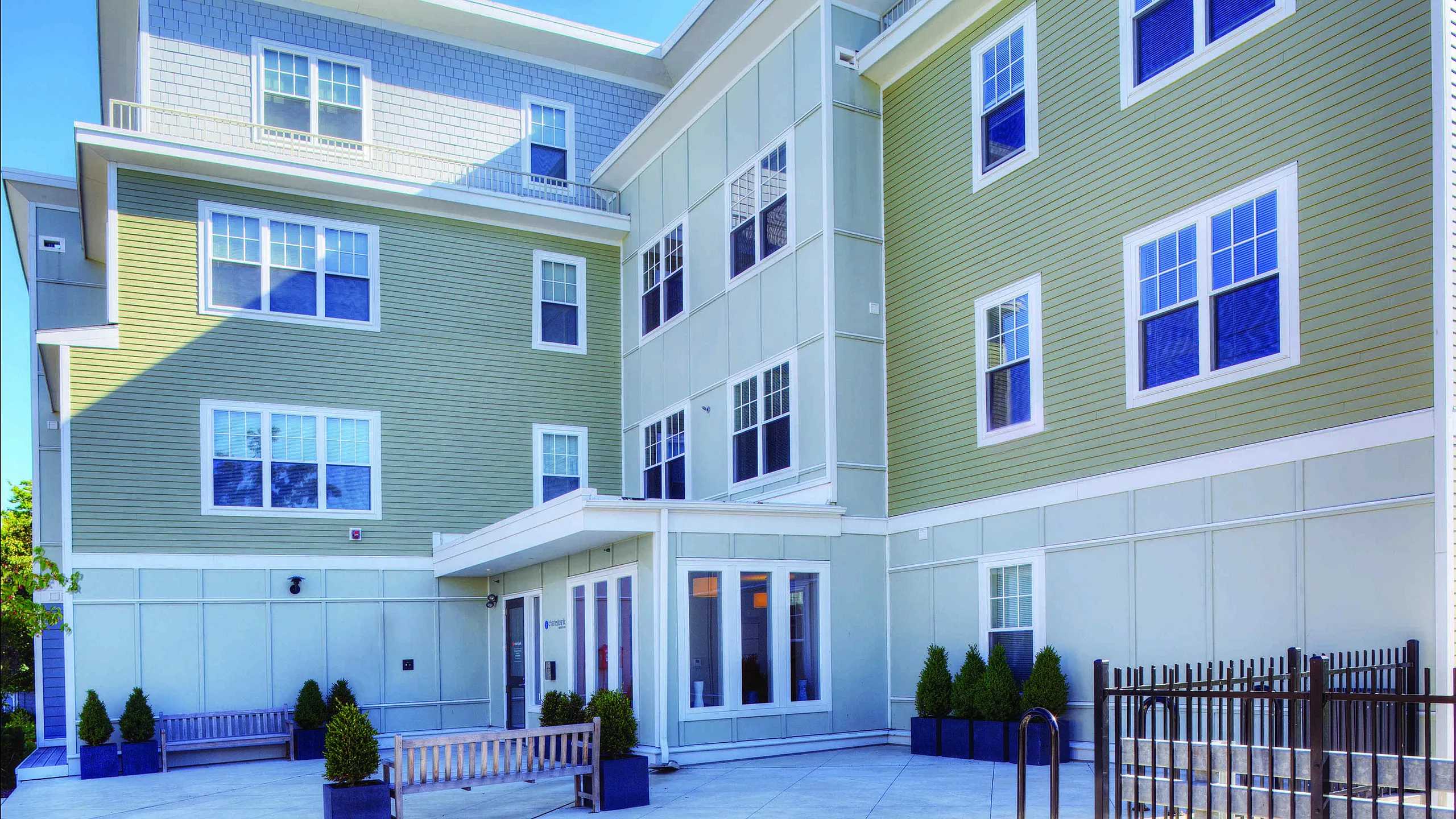 Modern apartment exterior showcasing elegant design with large windows, vibrant green siding, and a welcoming entrance area with benches and planters.