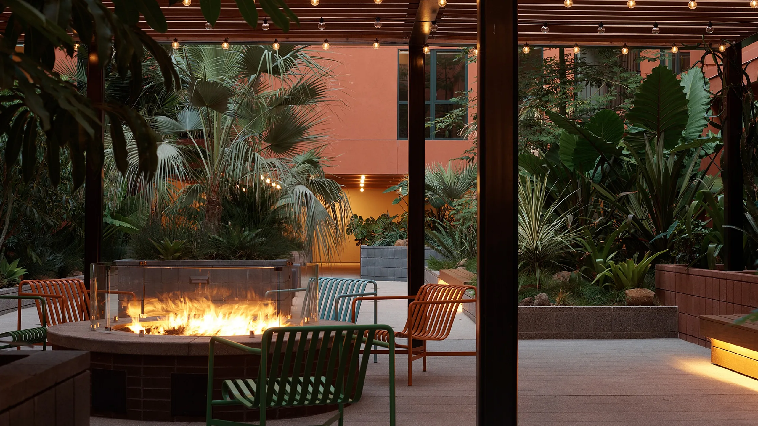 Chic outdoor patio with stylish seating around a cozy fire pit, surrounded by lush tropical plants and ambient string lighting.