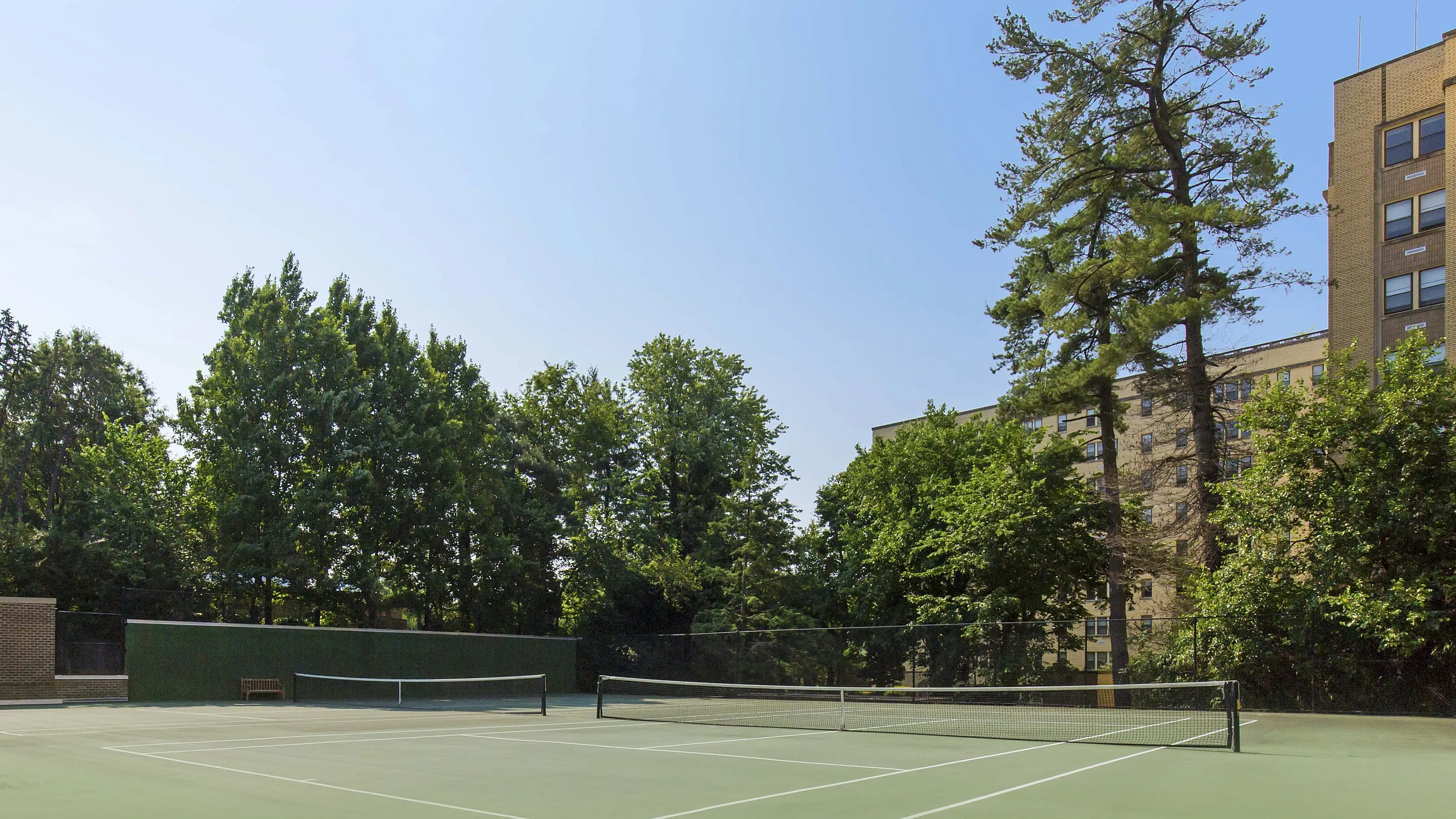 Sleek outdoor tennis court surrounded by lush greenery and an inviting residential building in the background.