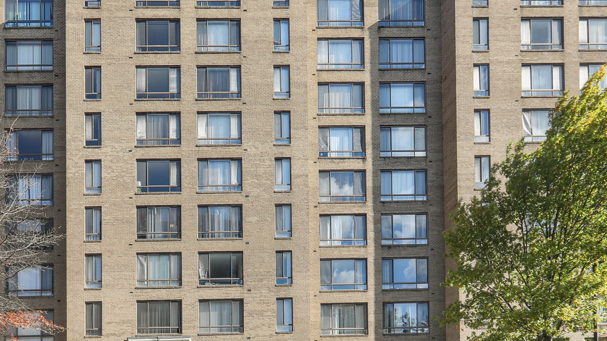 Elegant multi-story brick apartment building with large windows and modern entrance, surrounded by lush greenery.