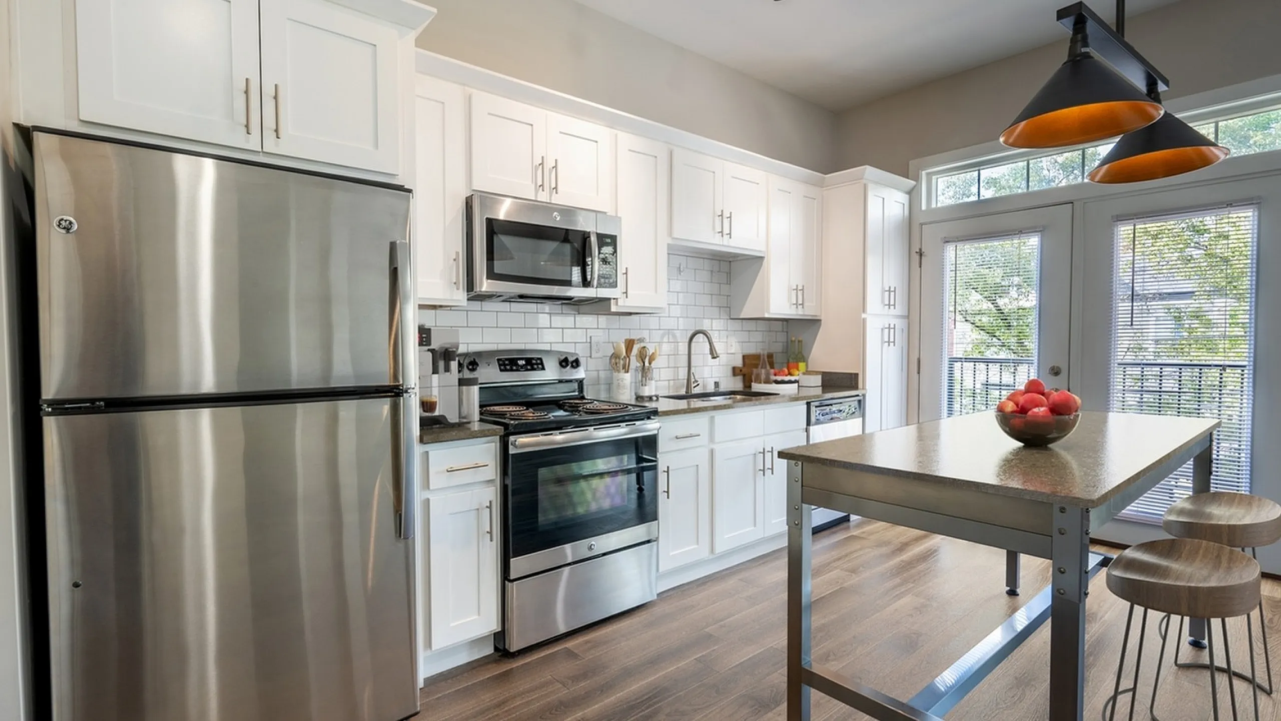 Modern kitchen with sleek stainless steel appliances, stylish white cabinetry, and a spacious island with bar stools under elegant pendant lighting.