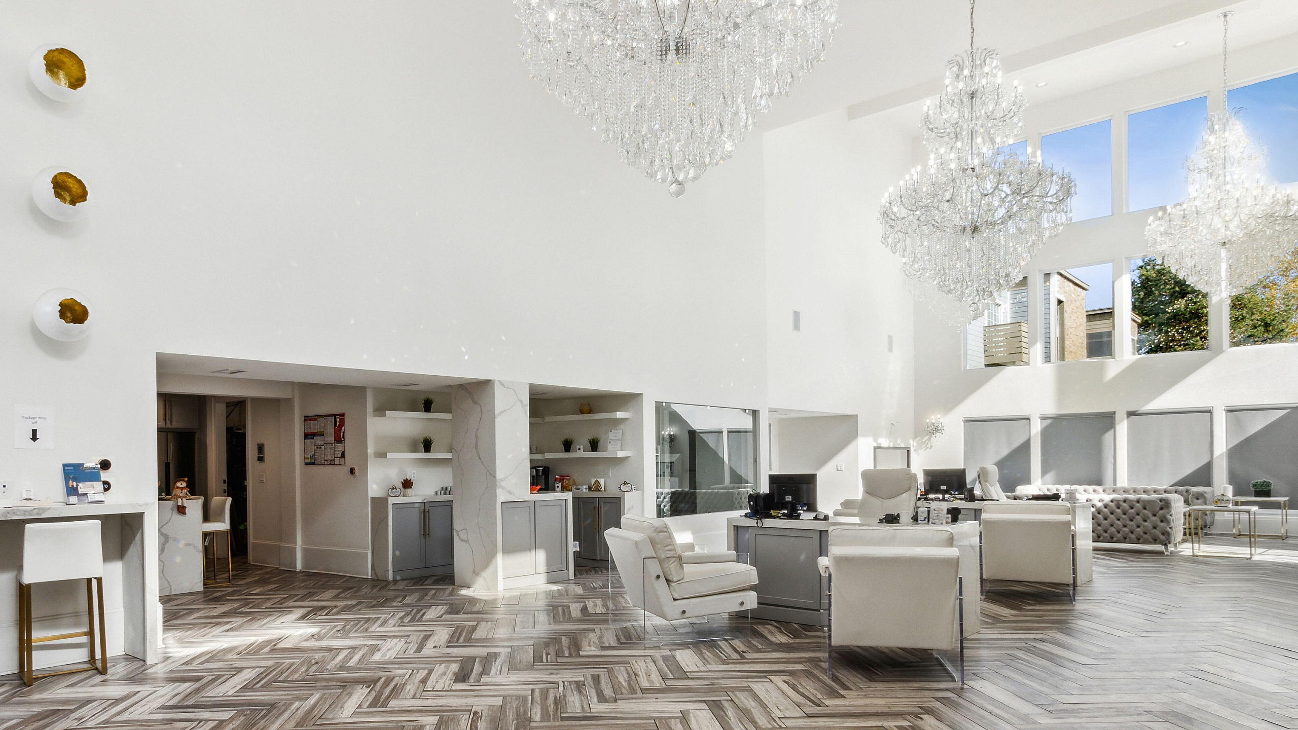Luxurious apartment interior showcasing an open space with elegant chandeliers, stylish herringbone flooring, and modern white furnishings under a vaulted ceiling.
