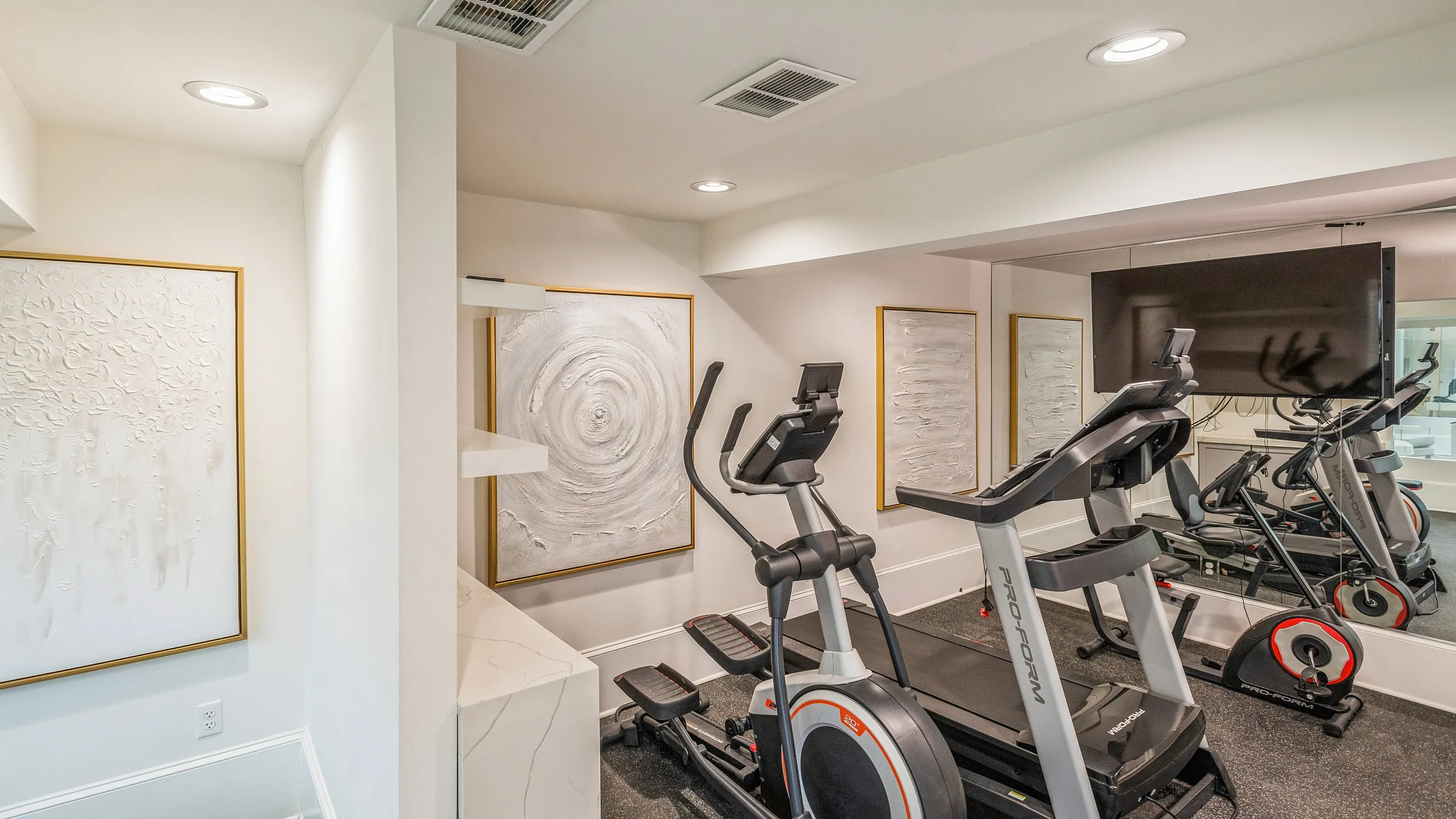 Modern home gym with exercise equipment, stylish artwork, and mirrored walls for a sleek workout space.