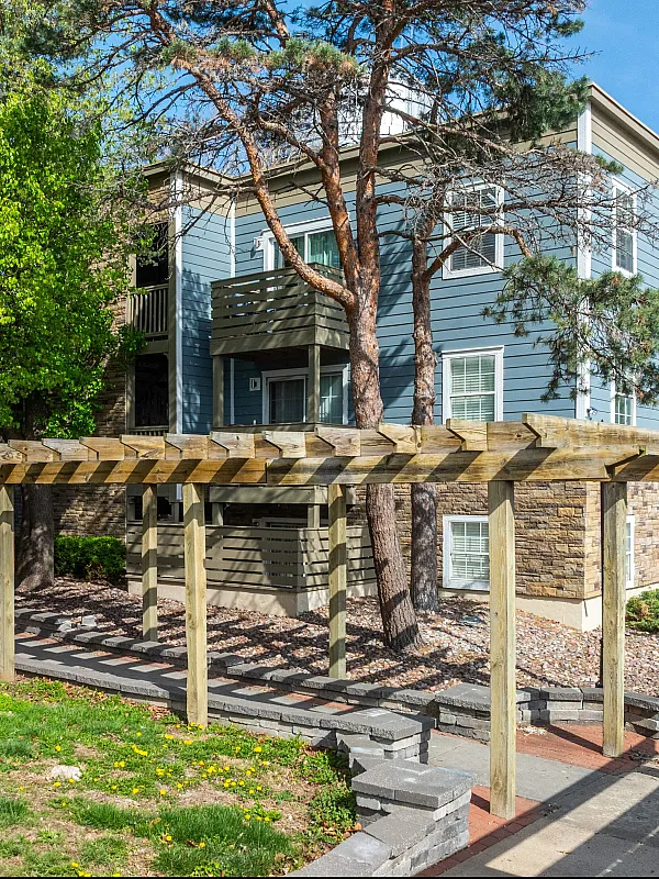 Charming apartment building with stone facade, lush greenery, and a scenic wooden pergola.