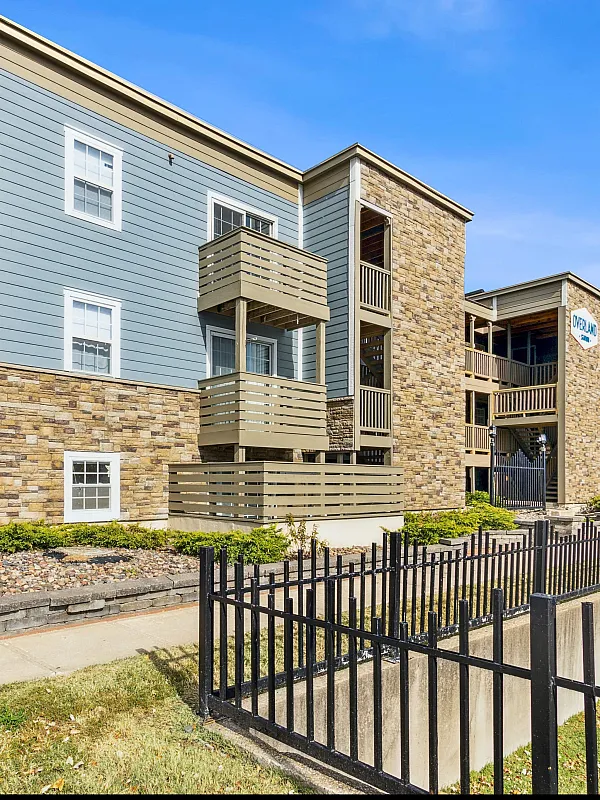 Charming apartment building with modern design featuring stone accents, balconies, and a fenced outdoor area under a clear blue sky.