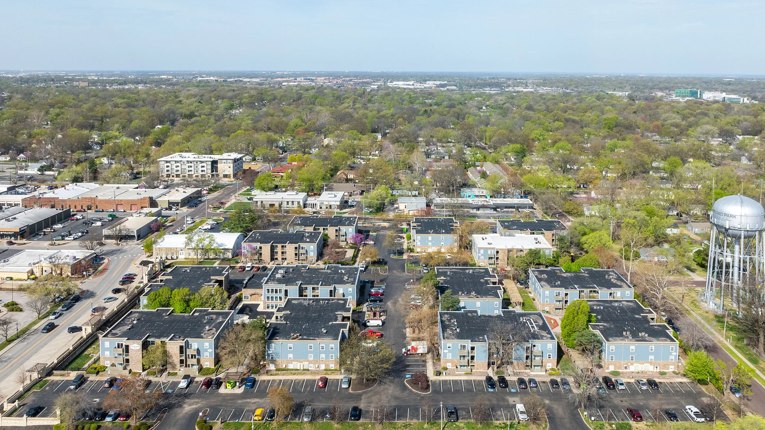 Aerial view of charming apartment complexes surrounded by lush greenery, ample parking, and vibrant community atmosphere.