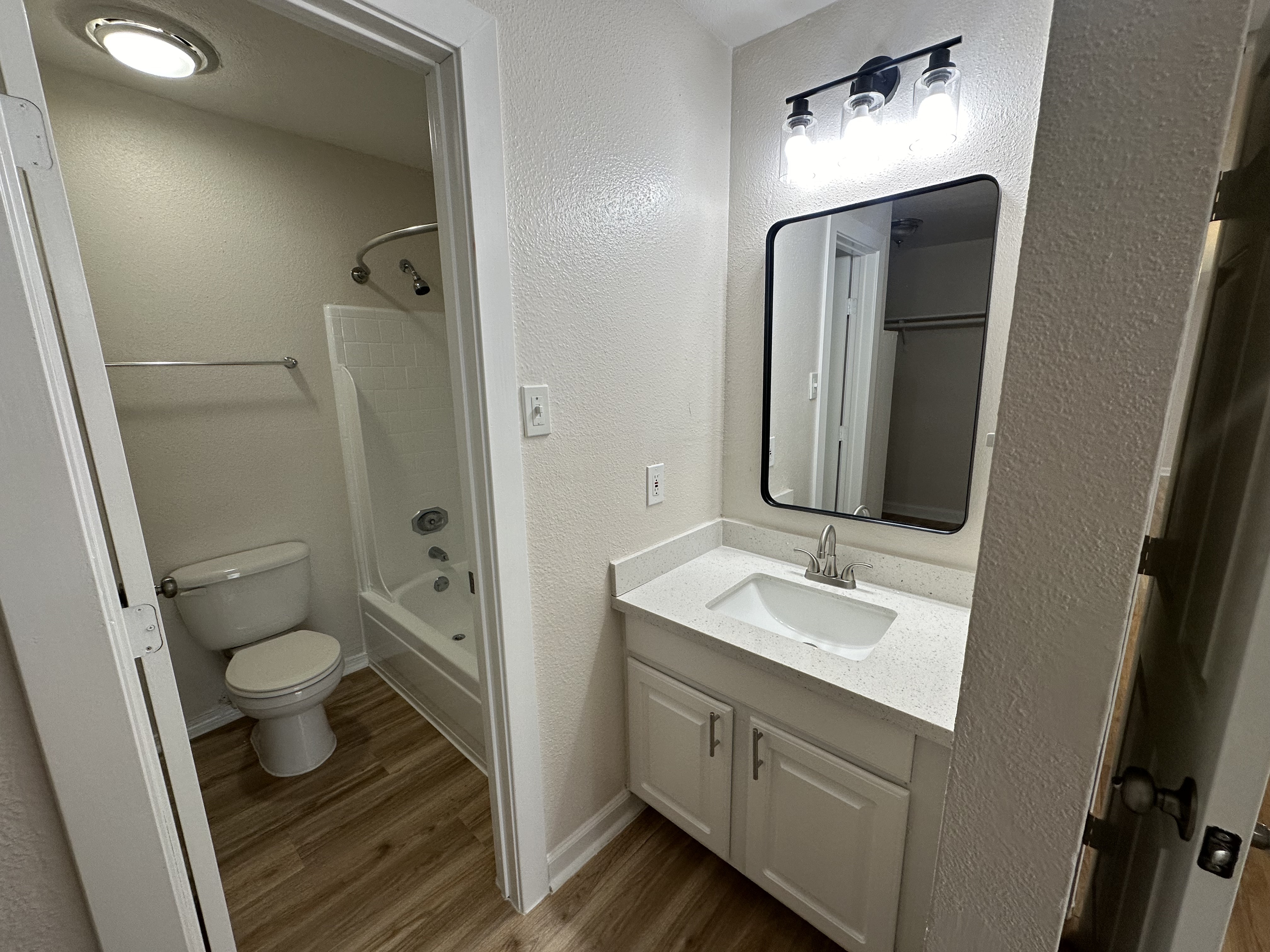 Modern bathroom with sleek vanity, large mirror, and stylish lighting above a bathtub and toilet.