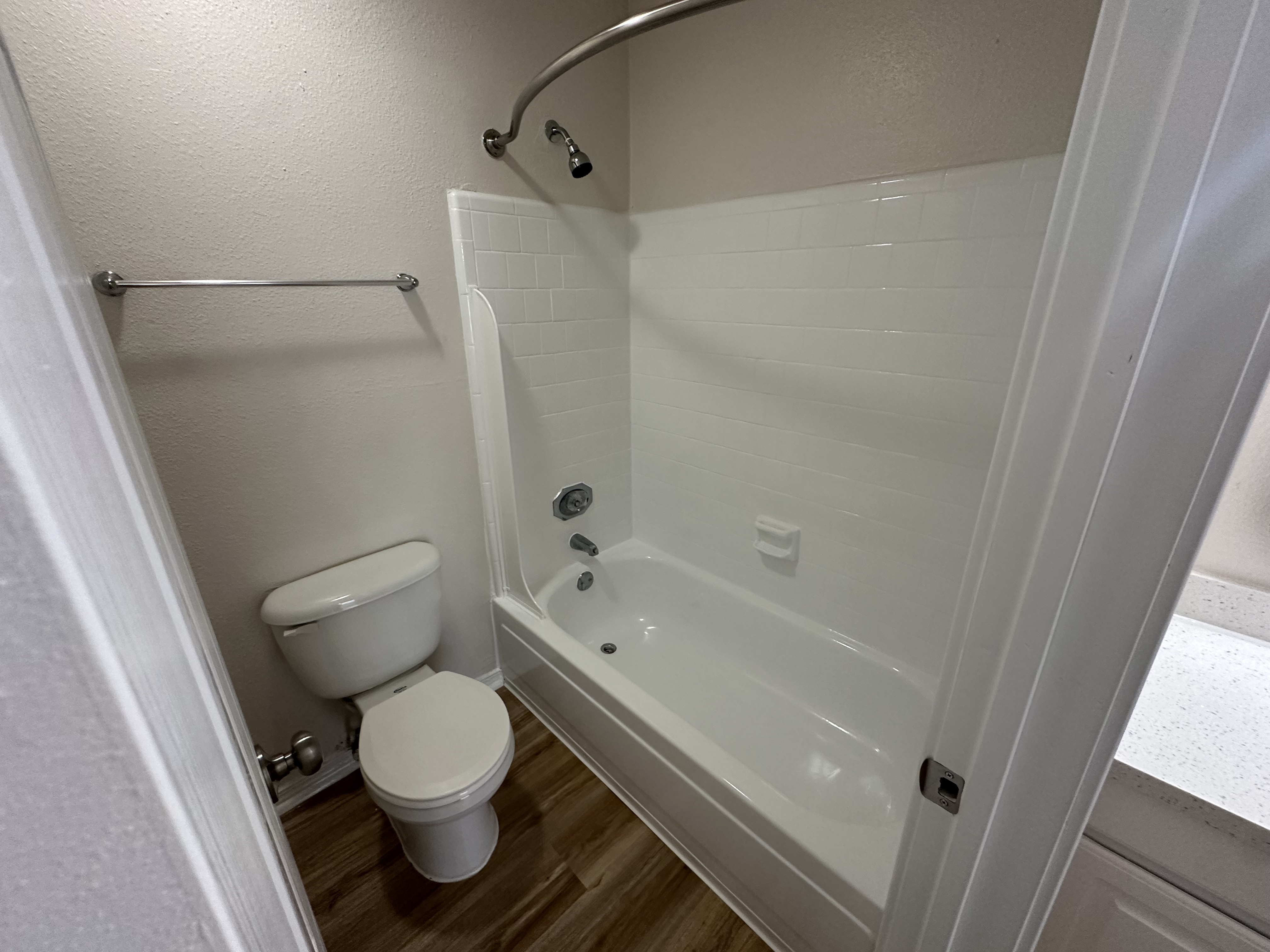 Modern bathroom featuring a sleek white shower-tub combo and elegant fixtures on wood-style flooring.