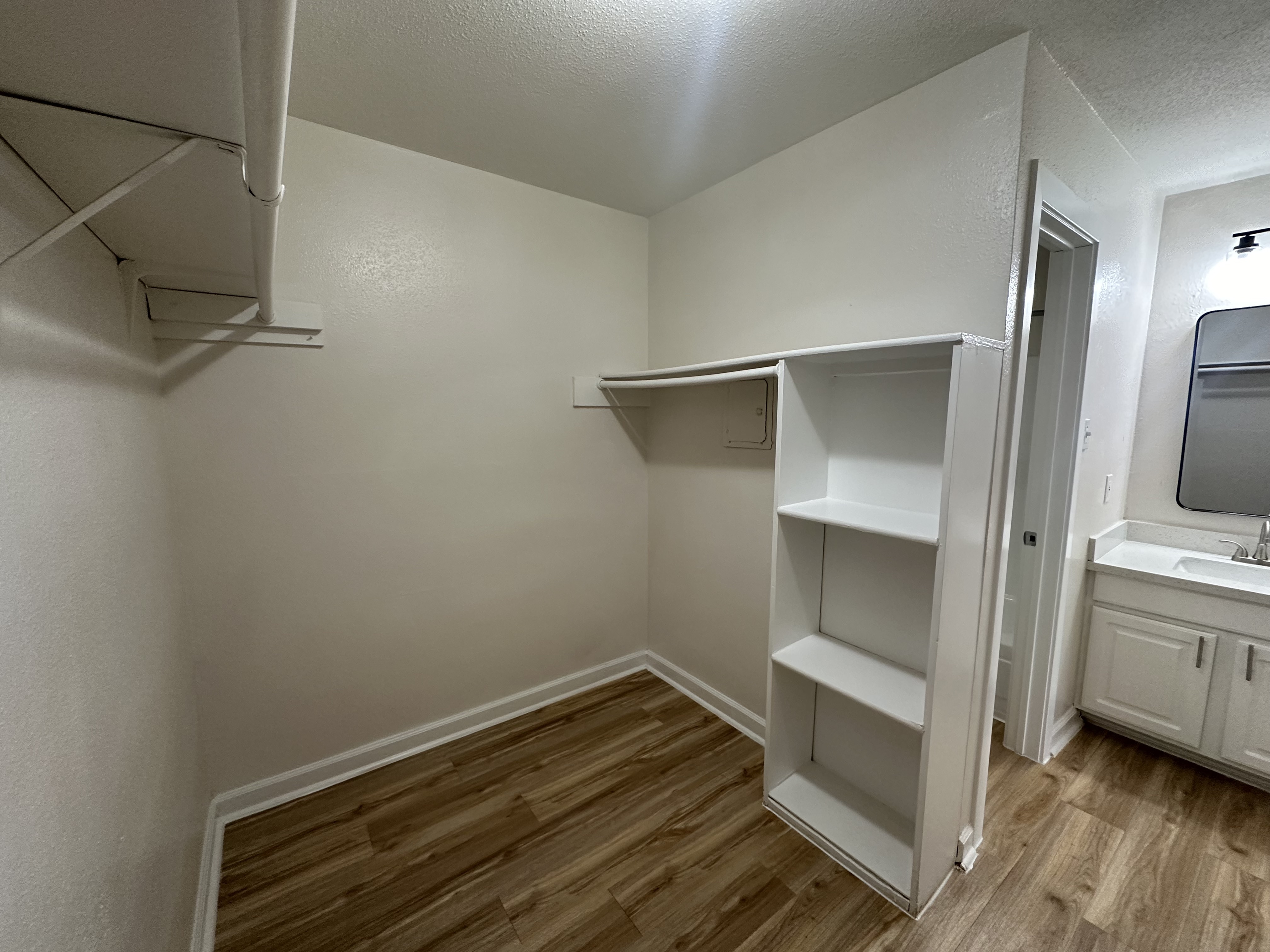 Spacious walk-in closet with sleek flooring, built-in shelving, and convenient access to a modern bathroom.