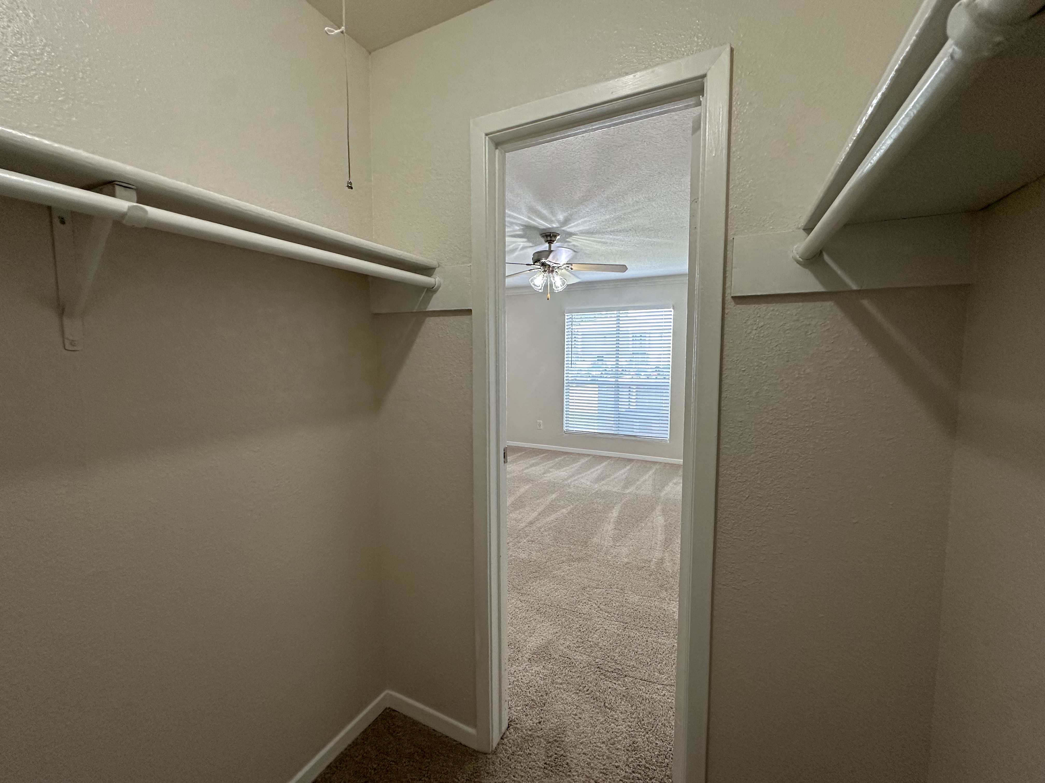 Bright walk-in closet leading to a carpeted bedroom with ceiling fan and natural light.