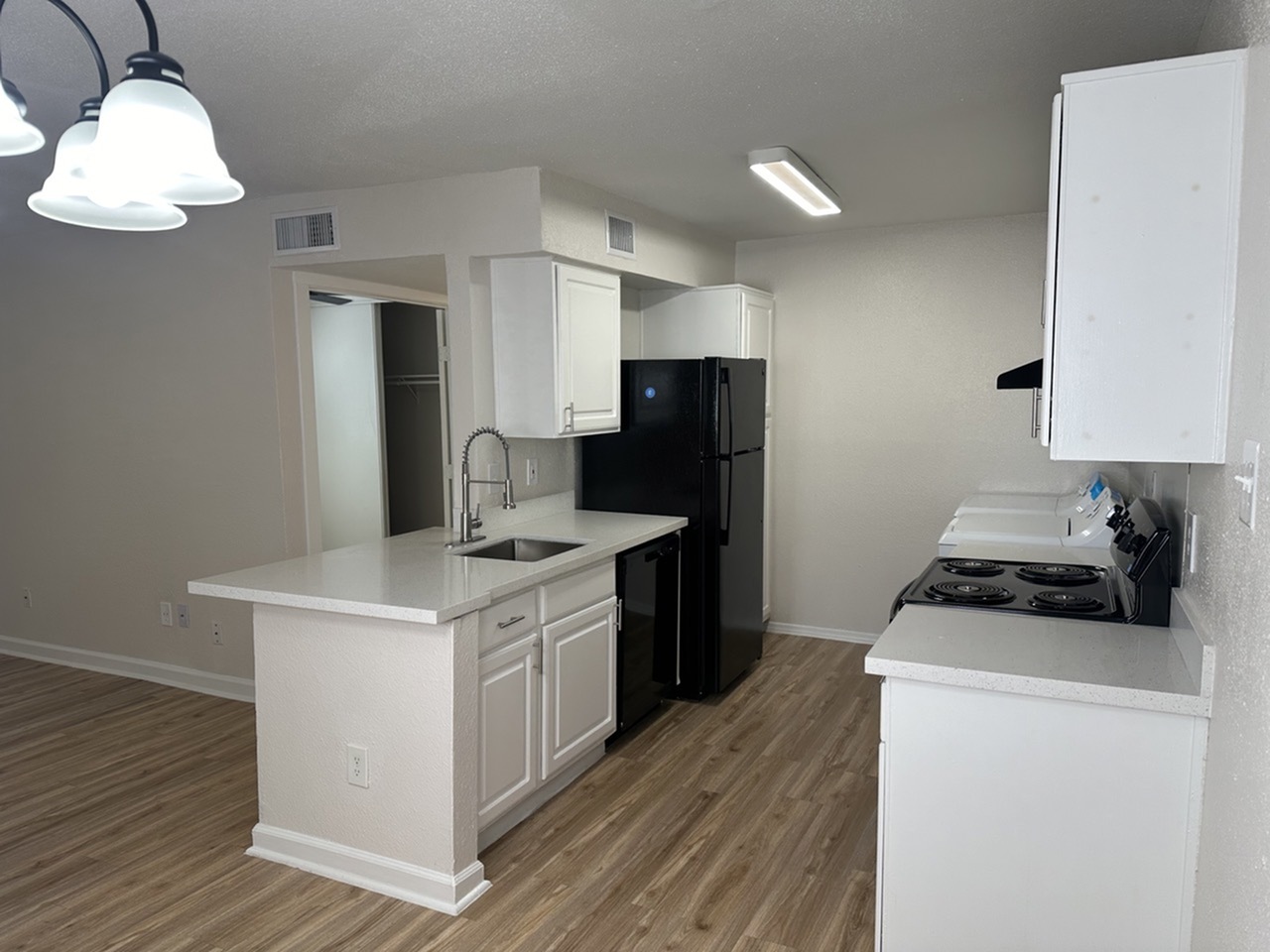 Modern kitchen with sleek black appliances, chic pendant lighting, and elegant white cabinetry on wood-style flooring.
