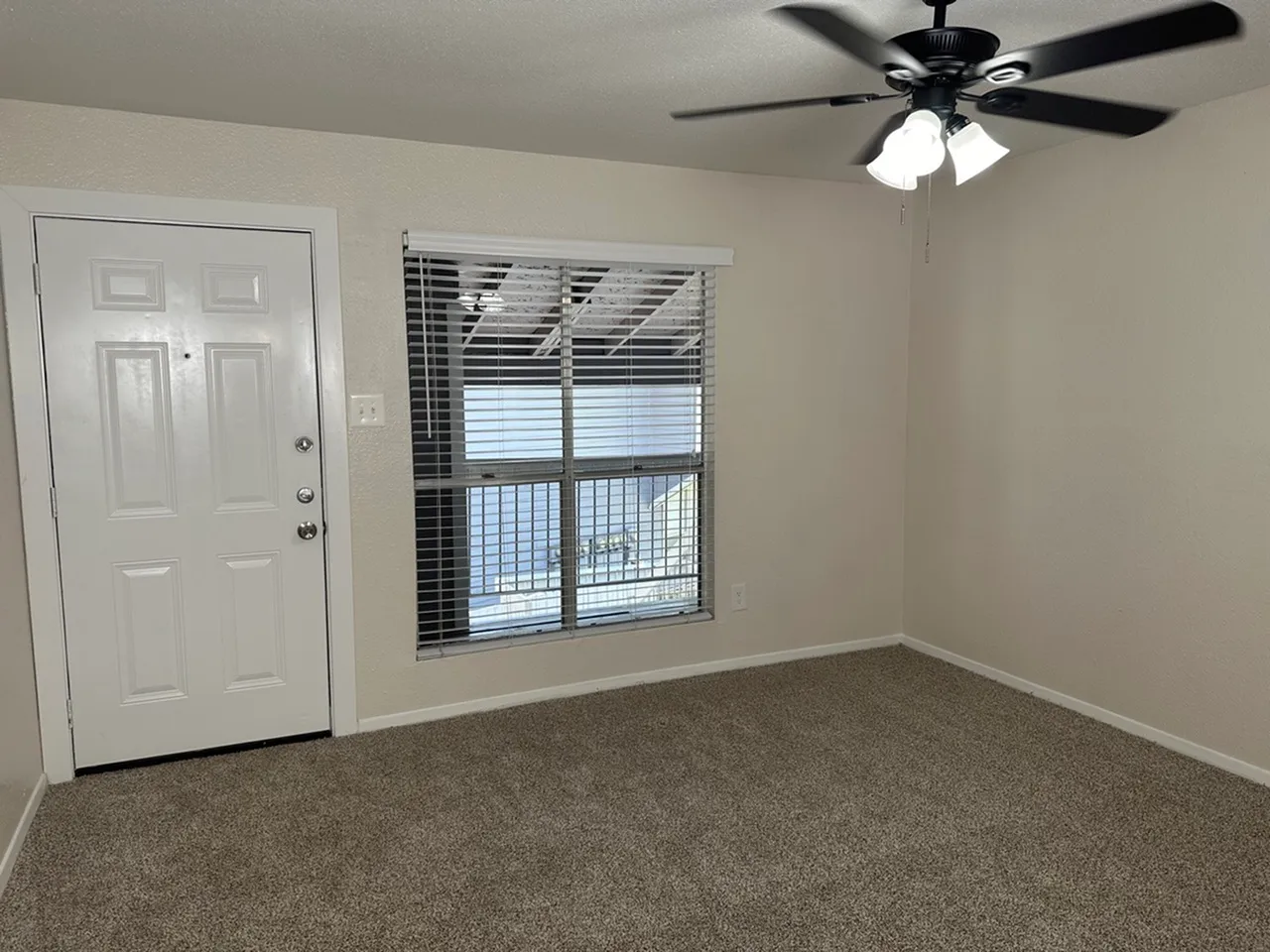 Inviting living space with carpeted floors, natural lighting from window with blinds, and stylish ceiling fan.