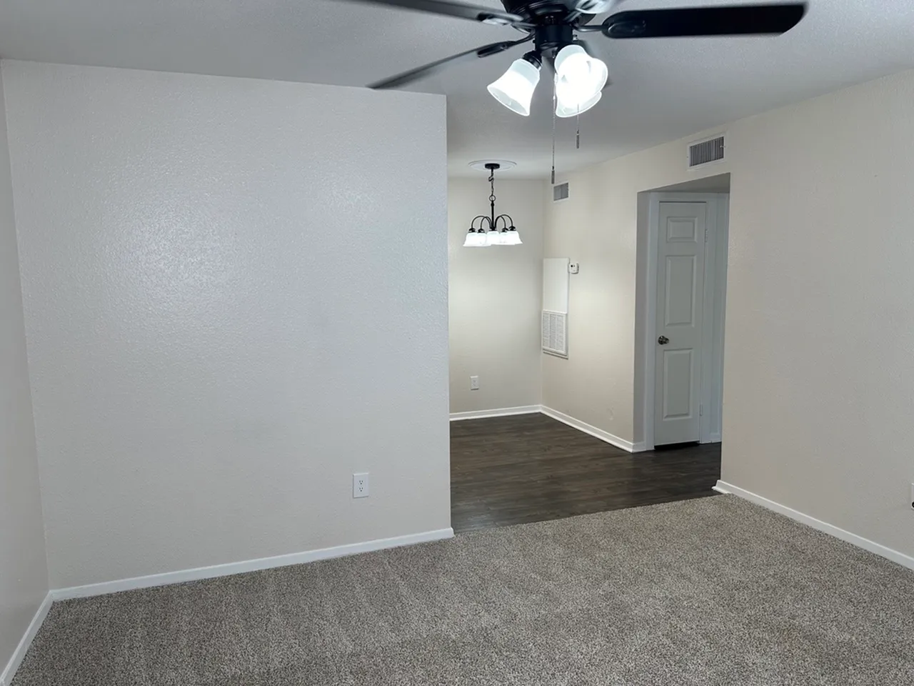 Inviting apartment interior featuring a cozy carpeted living area, elegant dark wood-style flooring, and a modern ceiling fan and lighting fixture.