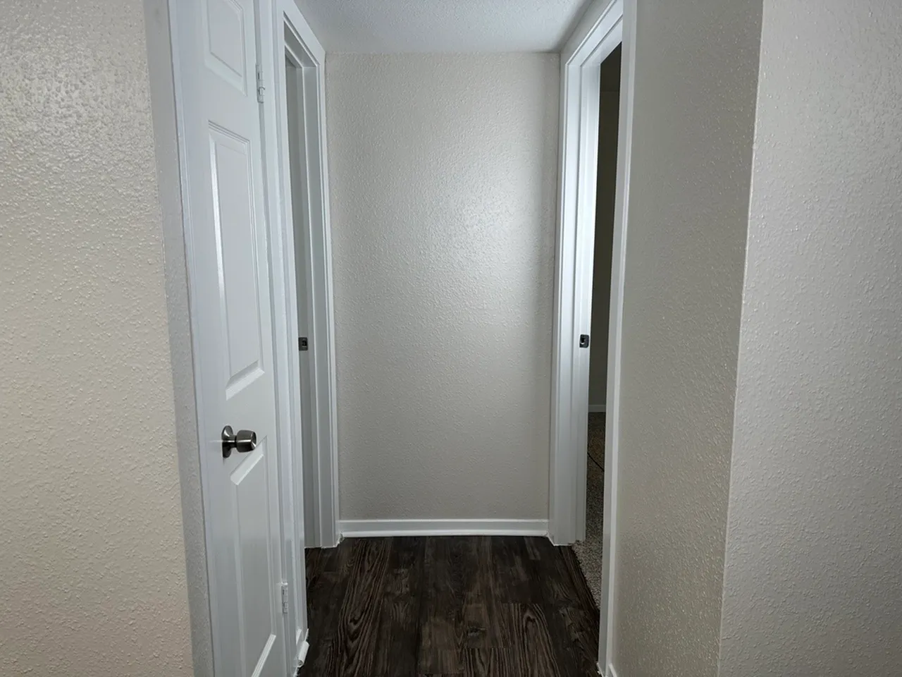 Modern hallway with crisp white doors and elegant wood flooring, leading to bedroom and bath.