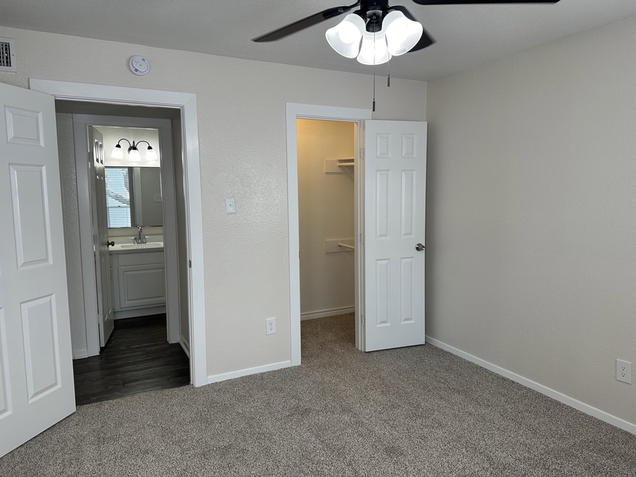 Bright bedroom with plush carpeting, featuring a ceiling fan, walk-in closet, and en-suite bathroom.