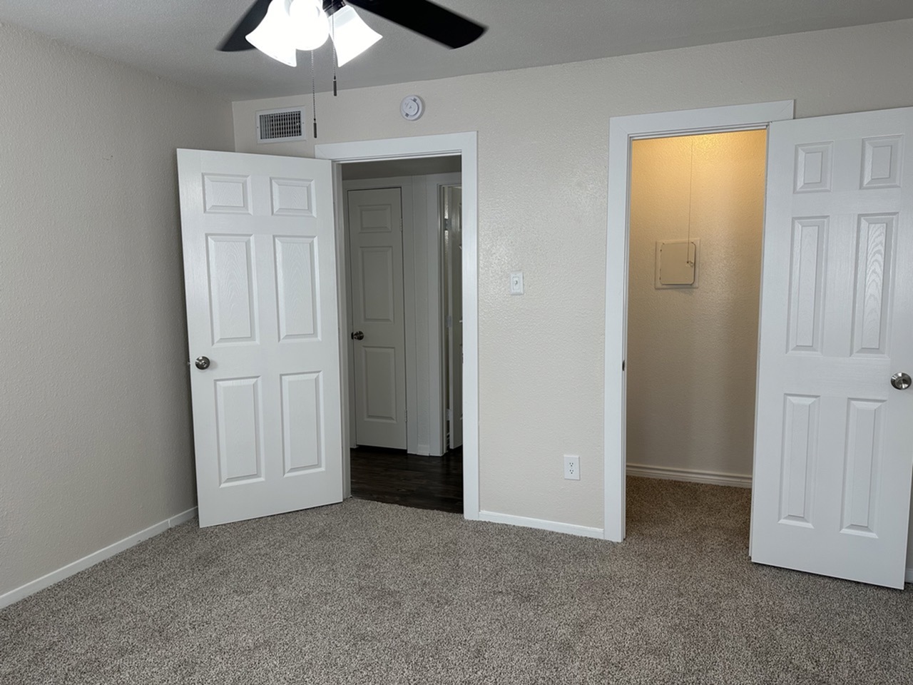 Bright and spacious bedroom with plush carpet, featuring dual doors and ceiling fan, in a modern apartment setting.