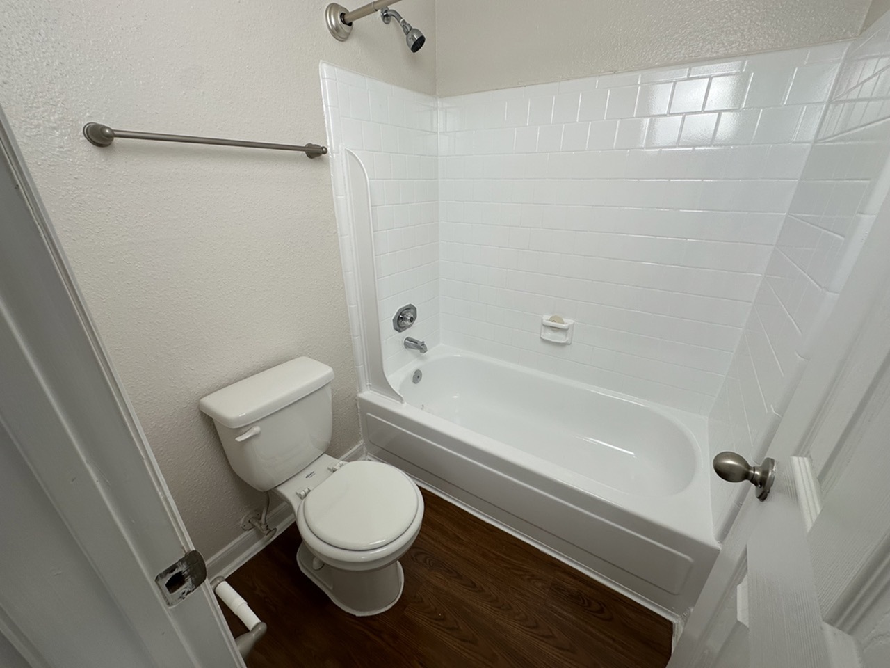 Modern bathroom featuring gleaming white tiles, a full tub, and stylish wood-style flooring.
