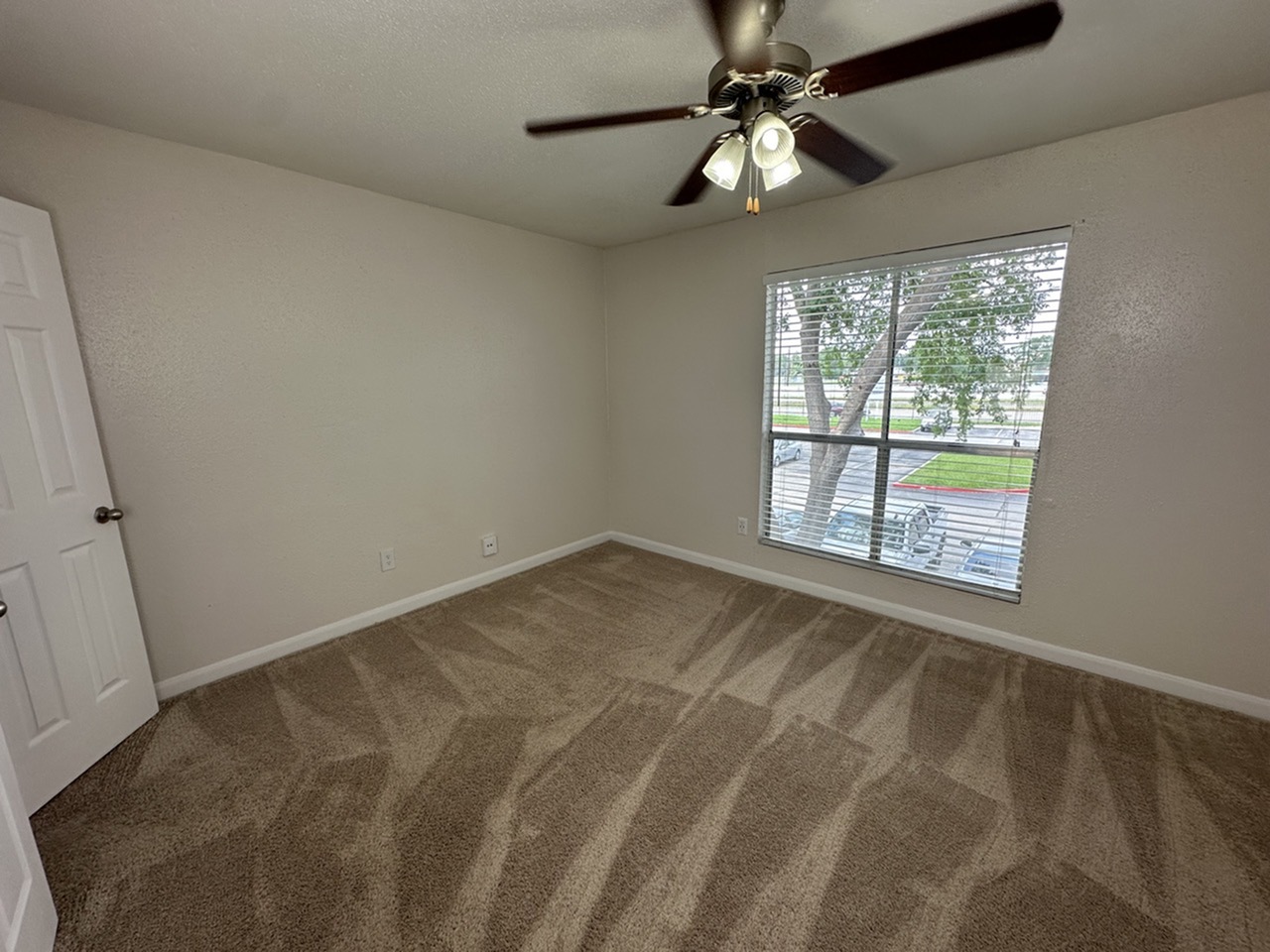 Bright, spacious bedroom featuring plush carpet, a ceiling fan, and a large window with a refreshing view.