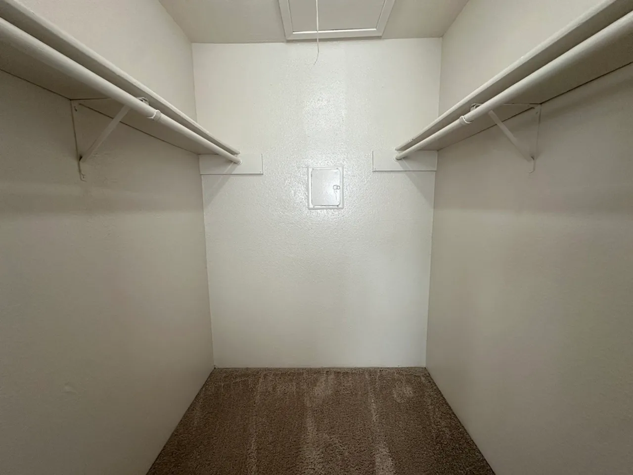 Spacious walk-in closet with dual hanging rods and clean white walls in a stylish apartment.