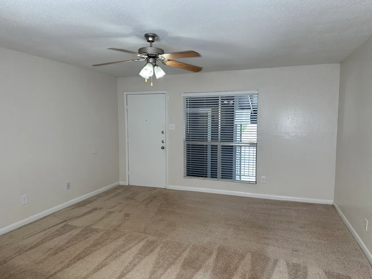 Inviting living room with plush carpet and natural light, featuring a ceiling fan and large window view.