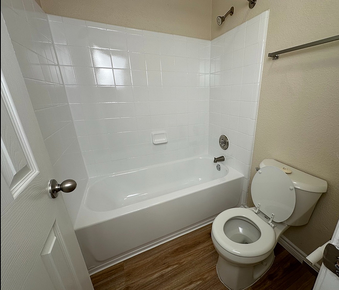 Modern bathroom featuring a sleek bathtub, pristine white tiles, and elegant wood flooring.