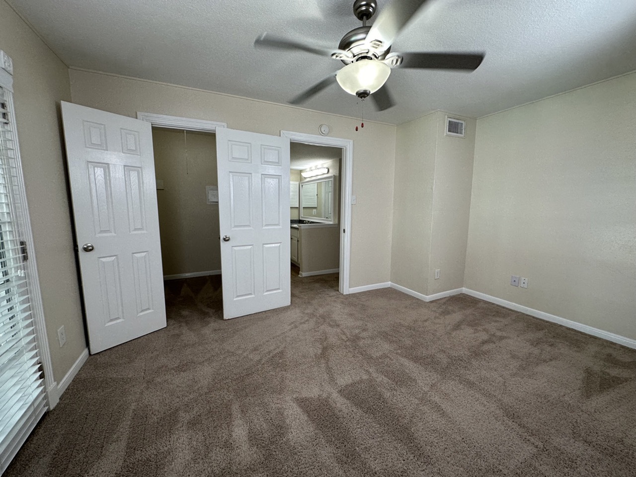 Inviting bedroom with plush carpeting, mirrored closet doors, and modern ceiling fan, offering comfort and style.