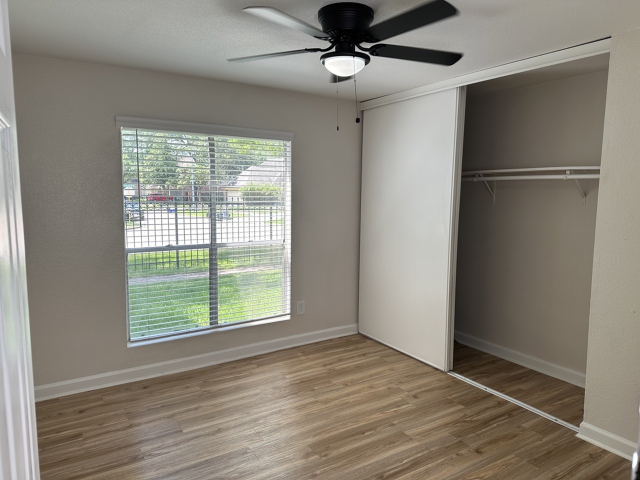 Bright and airy bedroom with sleek wooden floors, large window, and spacious closet, perfect for comfortable living.