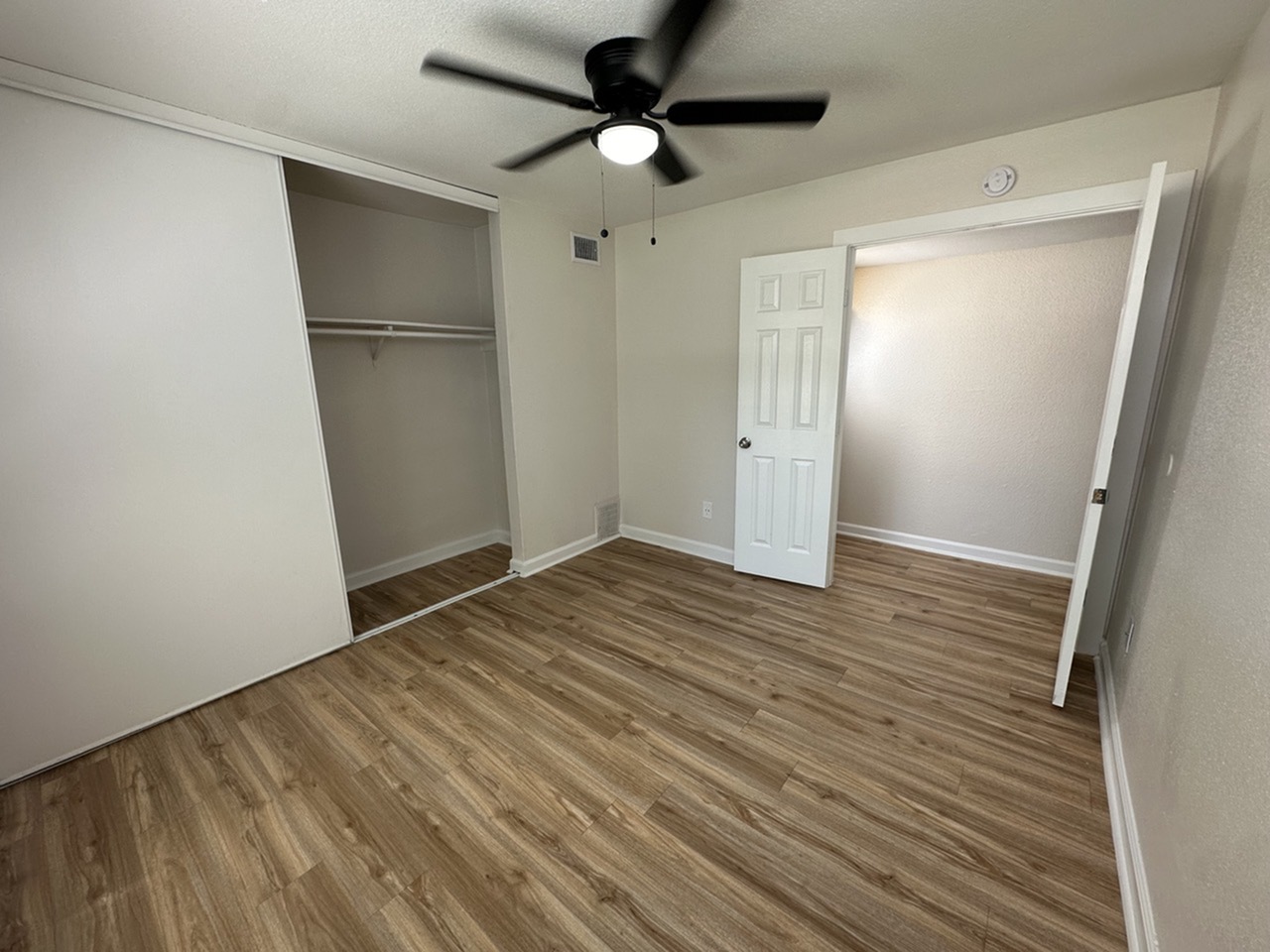Modern bedroom with elegant wood-style flooring, open closet space, and contemporary ceiling fan.