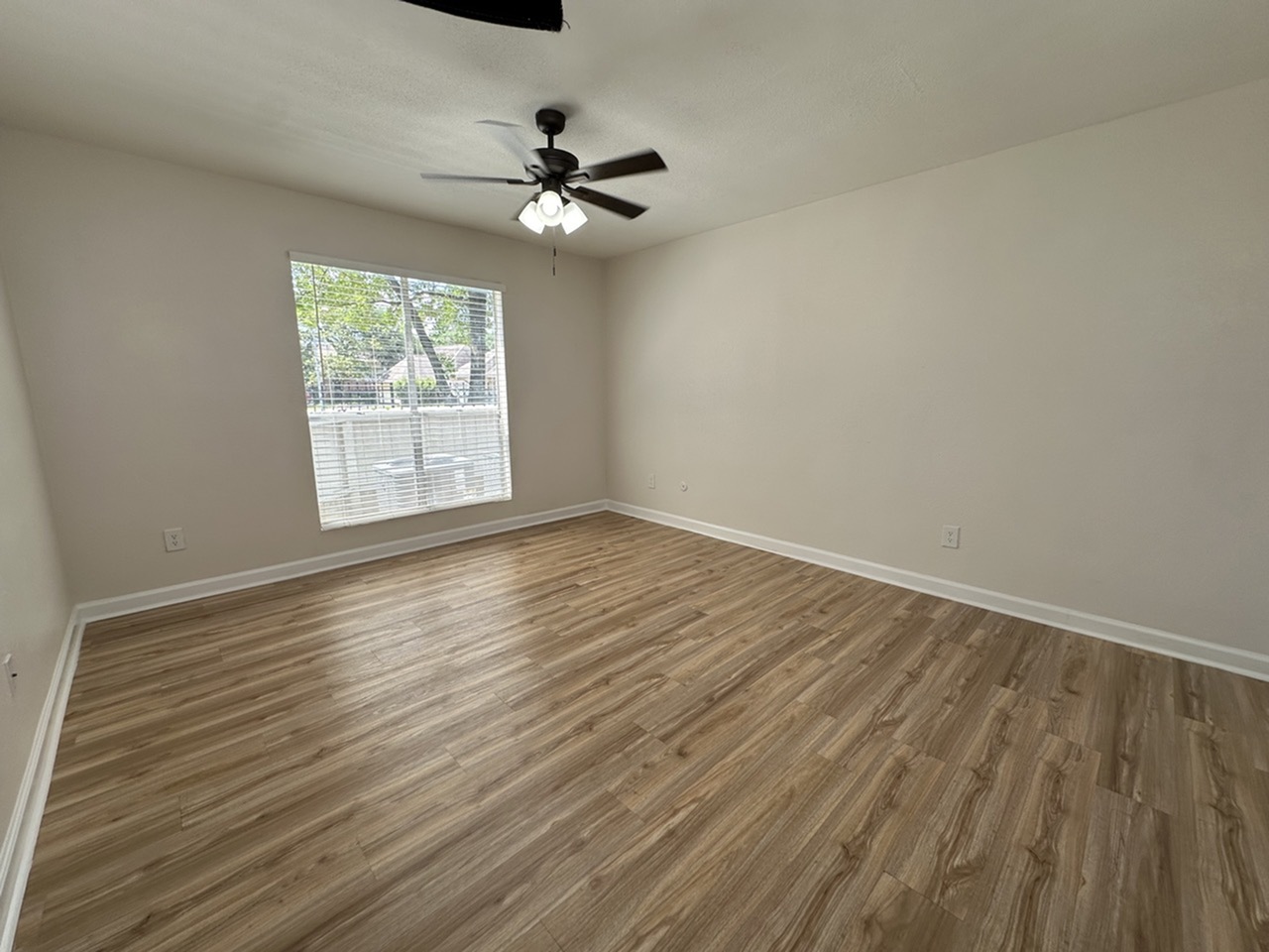 Bright and spacious room with elegant wood-style flooring, large window, and ceiling fan, perfect for comfortable living.