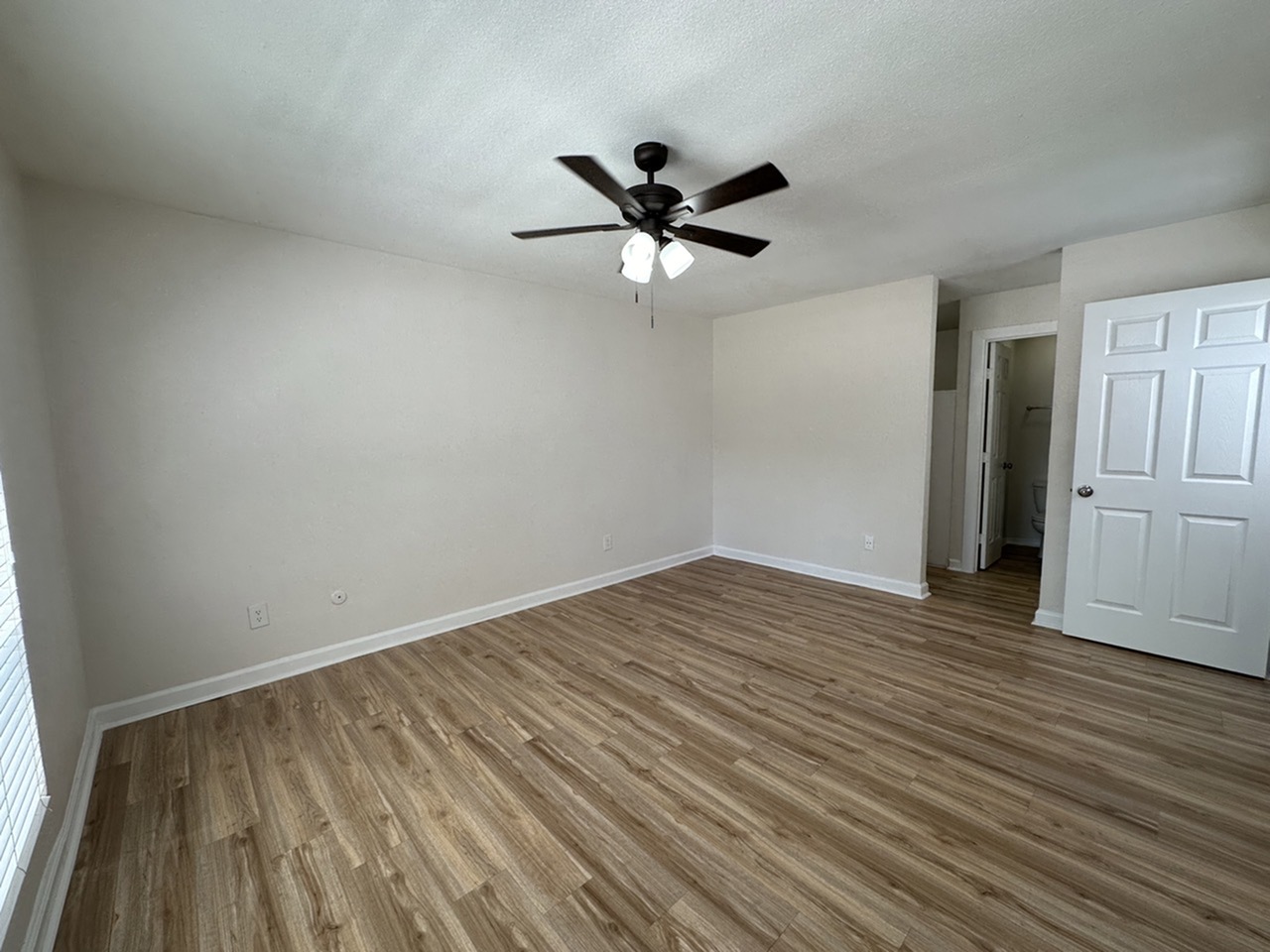 Spacious bedroom with elegant wood-style flooring, ceiling fan, and ample natural light.