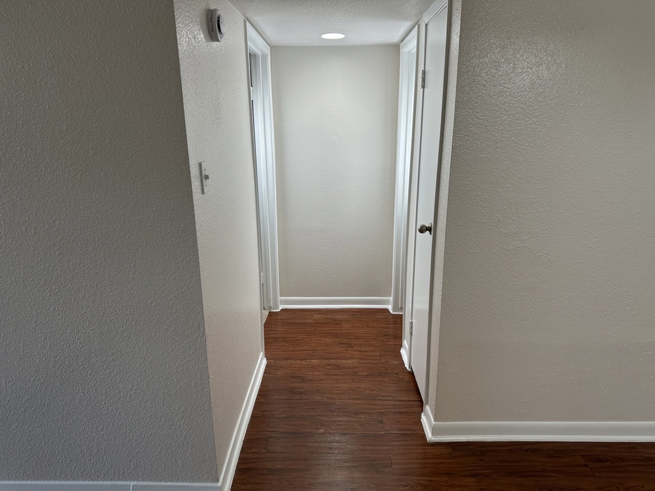 Bright hallway showcasing elegant wood-style flooring and sleek white trim, leading to bed and bathroom.