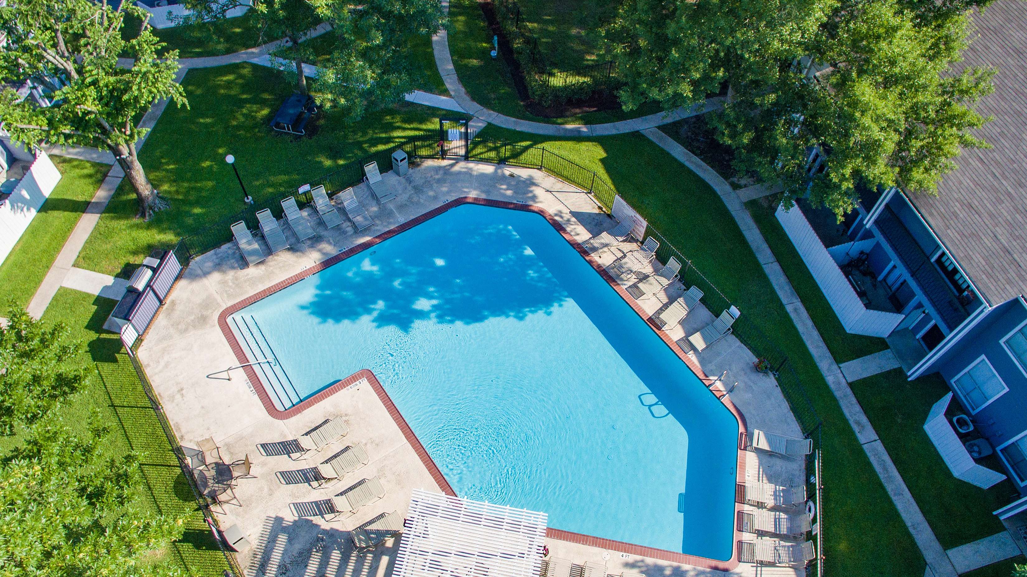 Aerial view of a beautifully landscaped apartment complex with a sparkling swimming pool, surrounded by lush greenery and inviting seating areas.