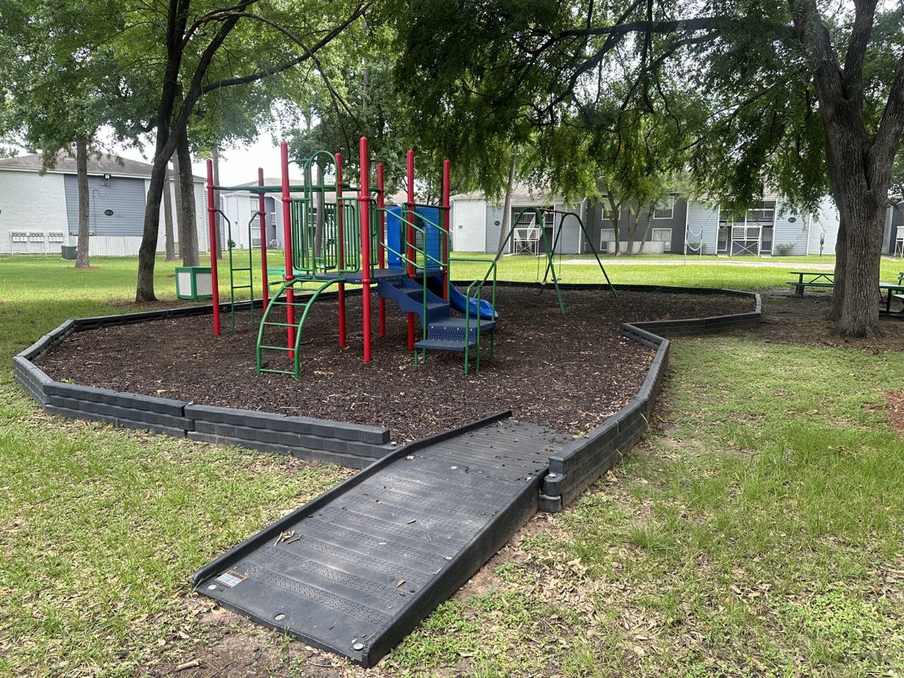 Charming outdoor playground with vibrant slides and swings nestled in a lush, green community setting.