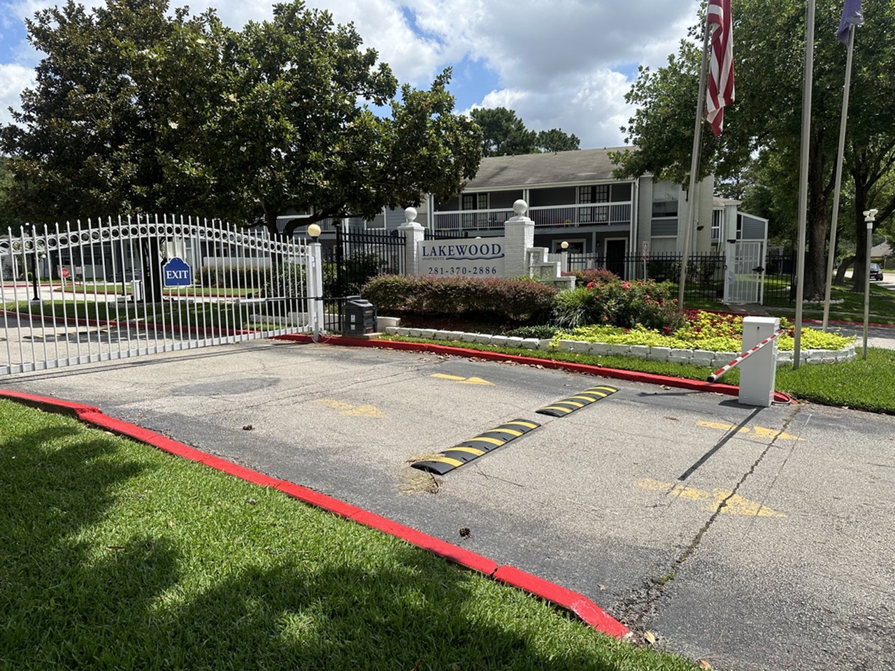 Charming gated entrance to Lakewood apartment complex, showcasing lush landscaping and a welcoming community sign under a clear blue sky.