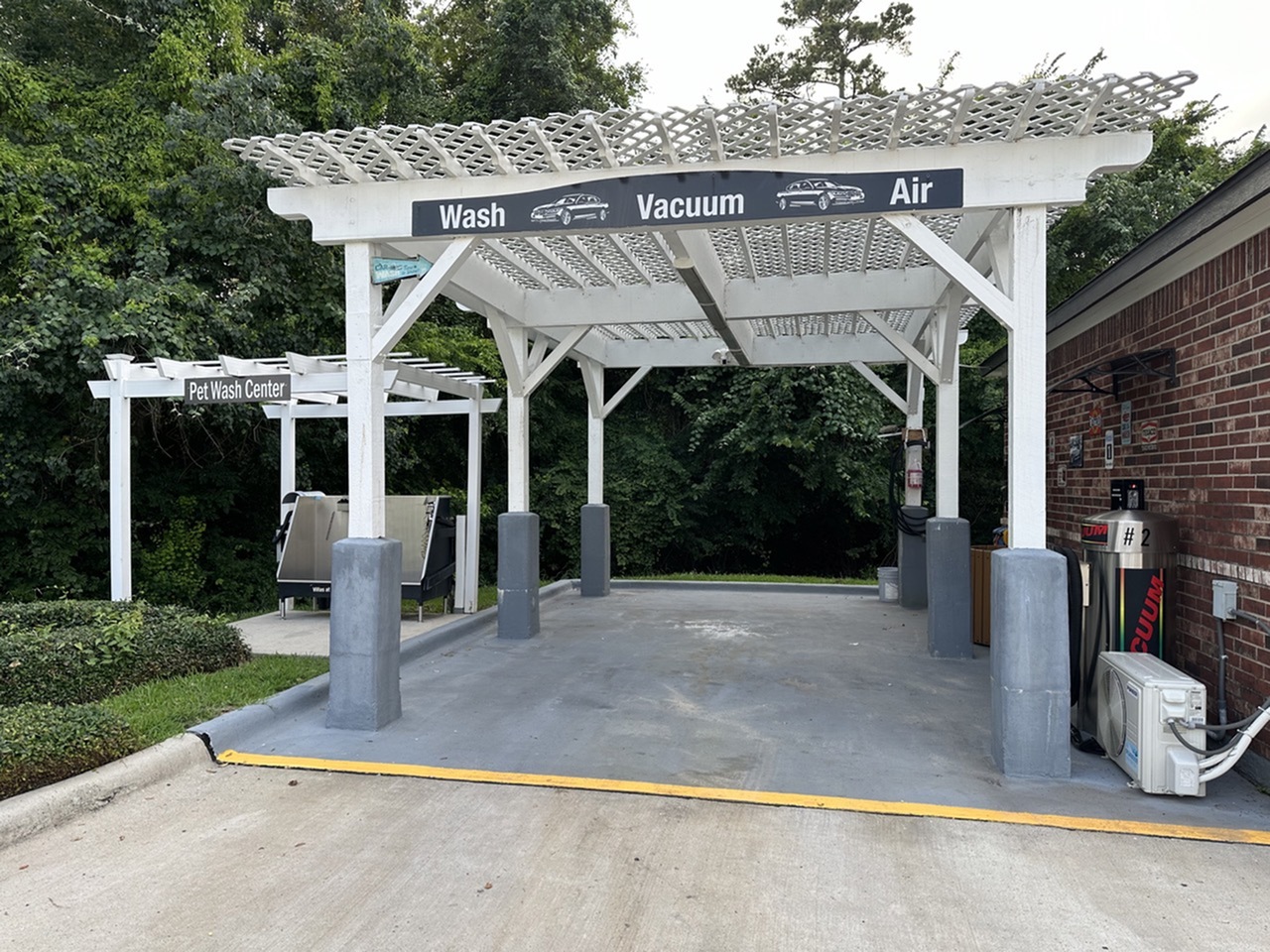 Convenient car wash area with vacuum and air services, adjacent to a pet wash center, surrounded by lush greenery.