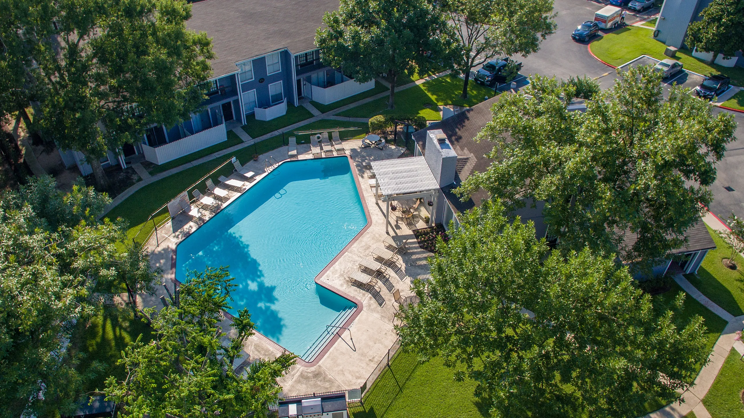 Aerial view of a modern apartment community with a sparkling pool, surrounded by lush greenery and inviting lounge chairs, perfect for relaxation and leisure.