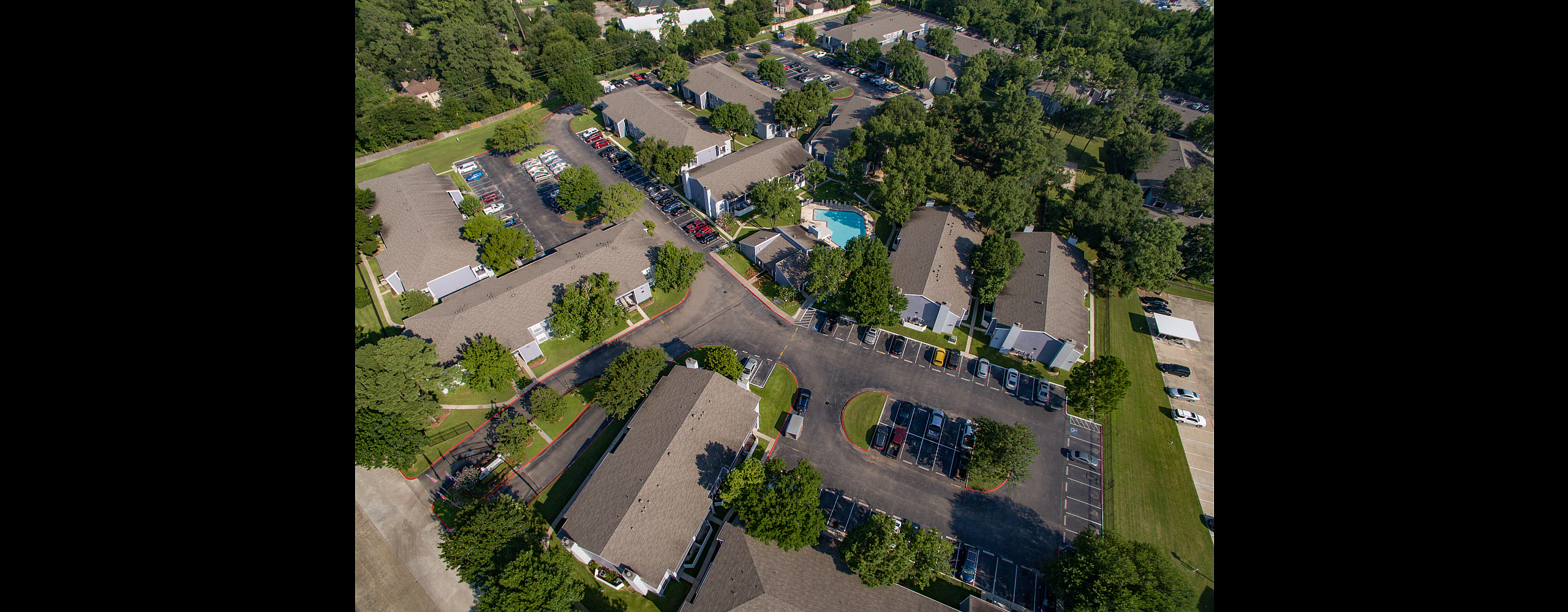 Vibrant aerial view of a modern apartment complex with lush greenery, ample parking, and a refreshing swimming pool.