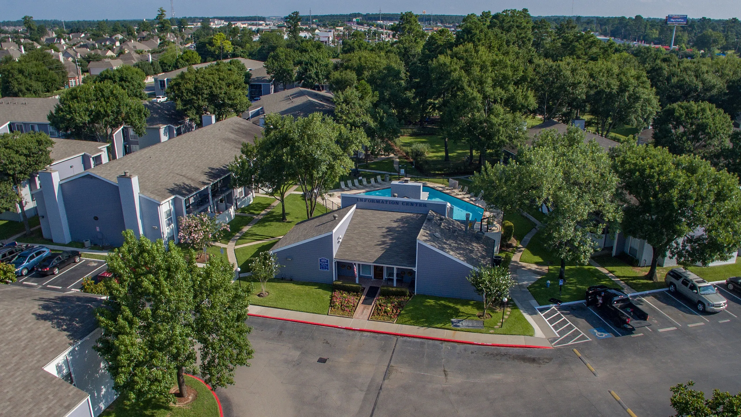 Aerial view of a charming residential community with lush greenery, inviting pool area, and ample parking facilities.