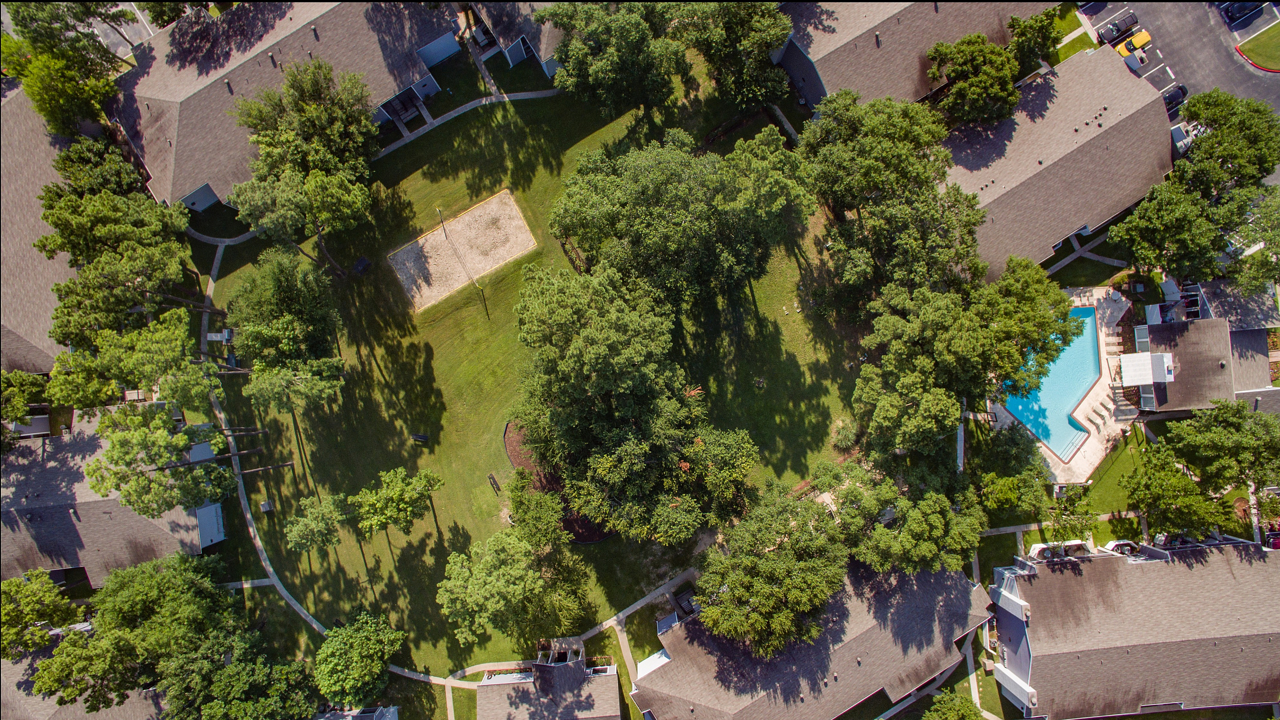 Aerial view of a lush residential complex with inviting pool, surrounded by green lawns and mature trees, offering a tranquil and scenic living environment.