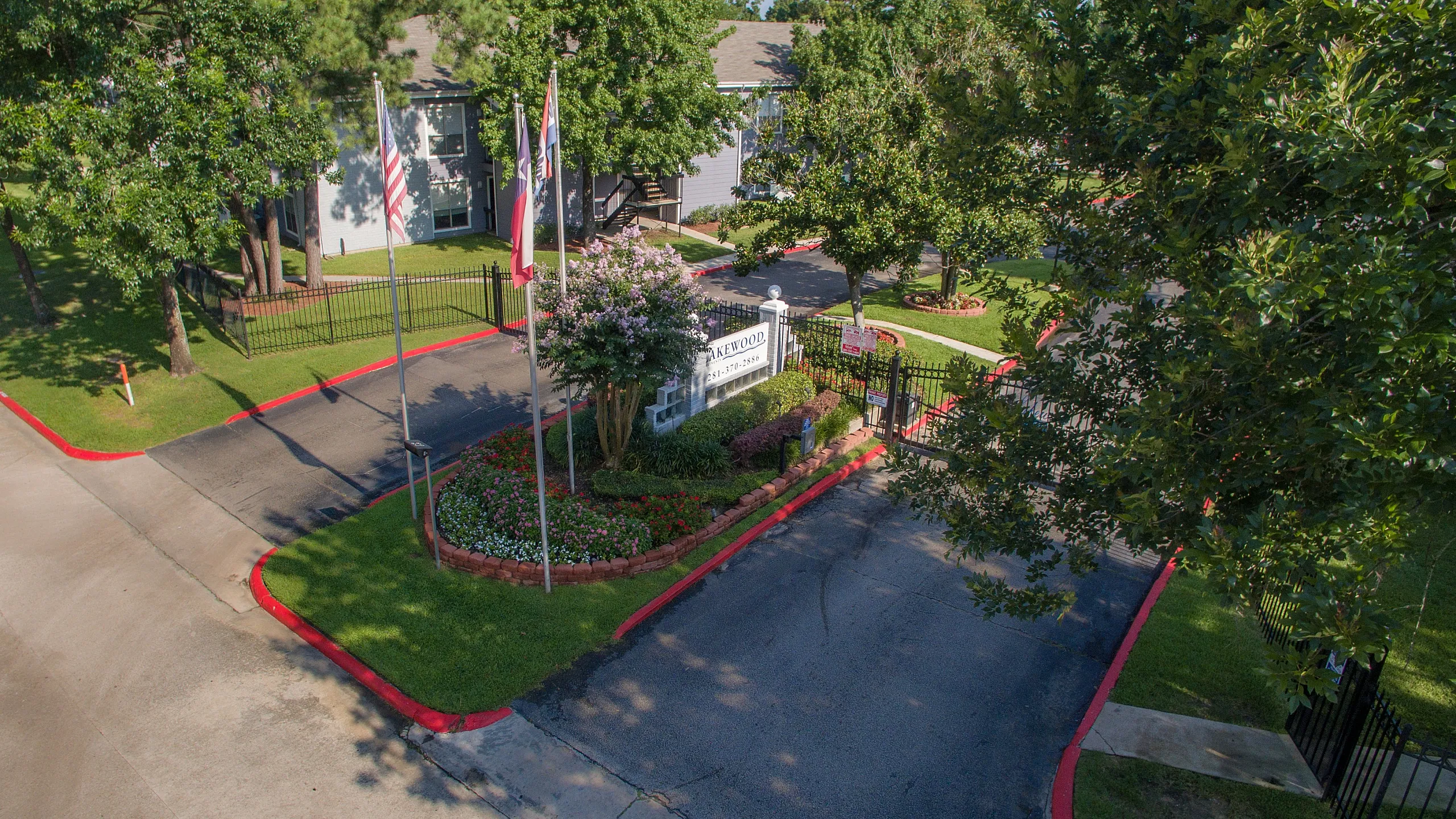 Charming gated apartment entrance and exit with lush landscaping and vibrant flags, offering a welcoming and secure environment.