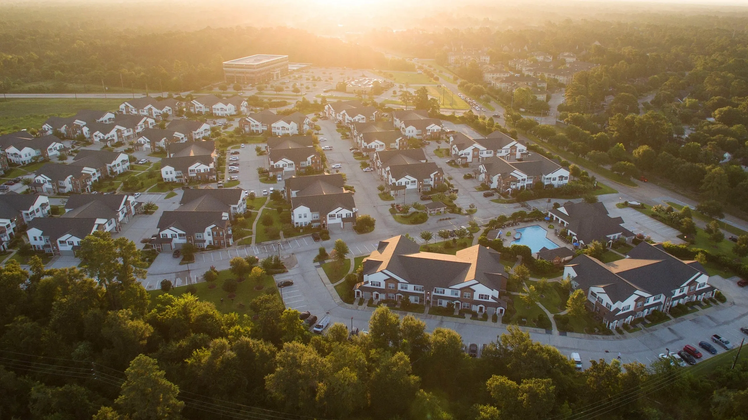 Charming aerial view of a spacious, lush apartment complex at sunset, featuring a serene landscape and a sparkling pool.