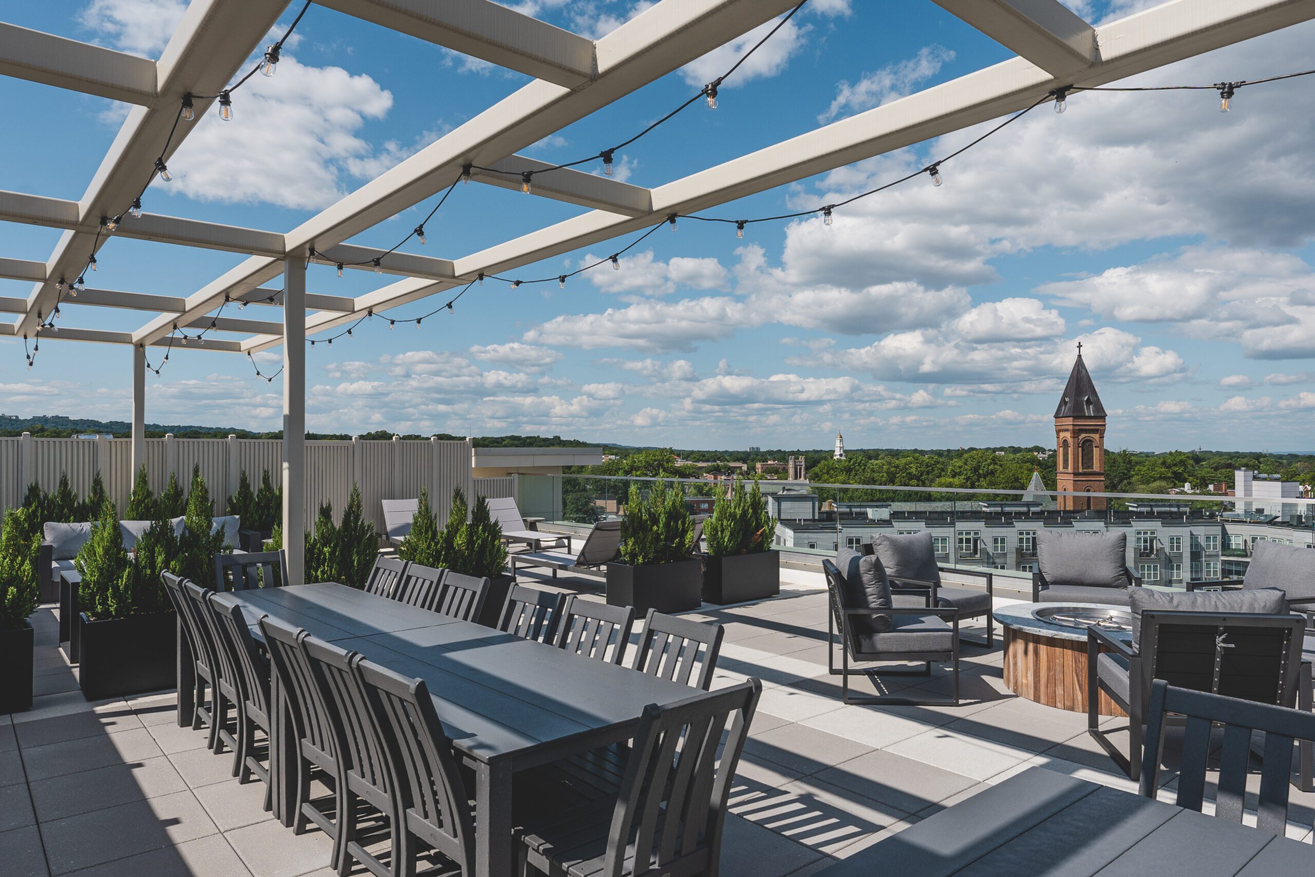 Luxurious rooftop terrace with elegant seating, vibrant greenery, and panoramic city views under a sunny sky.