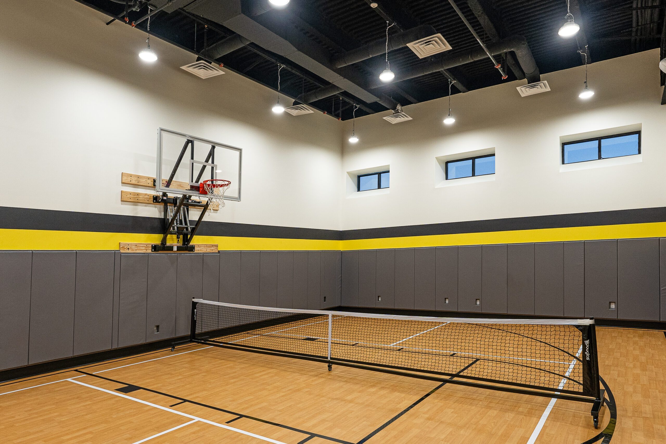 Modern indoor sports court featuring a basketball hoop and versatile floor for multiple games, enhanced by bright lighting and stylish design.