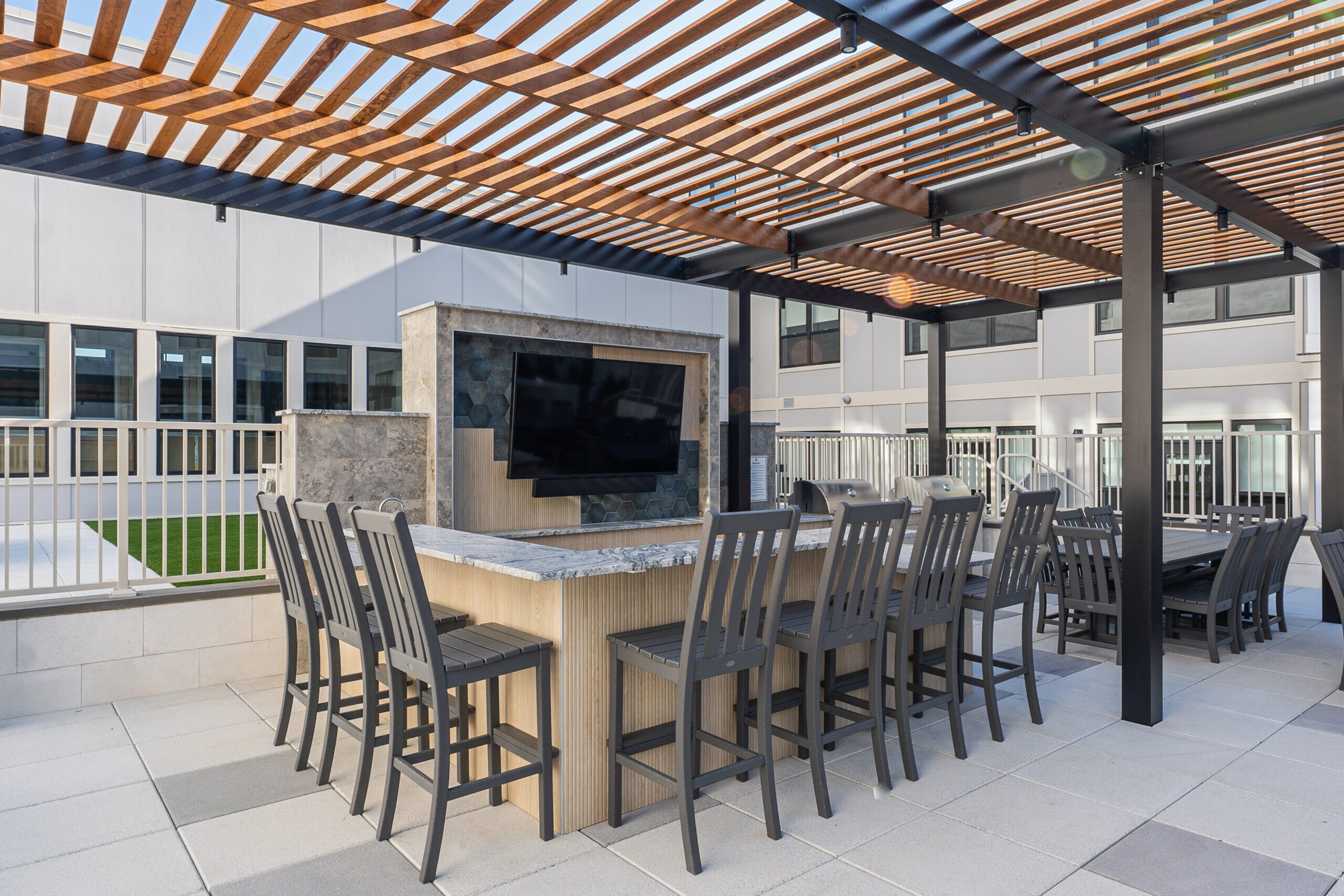 Modern outdoor patio with sleek bar seating and a large TV under a stylish wooden pergola.