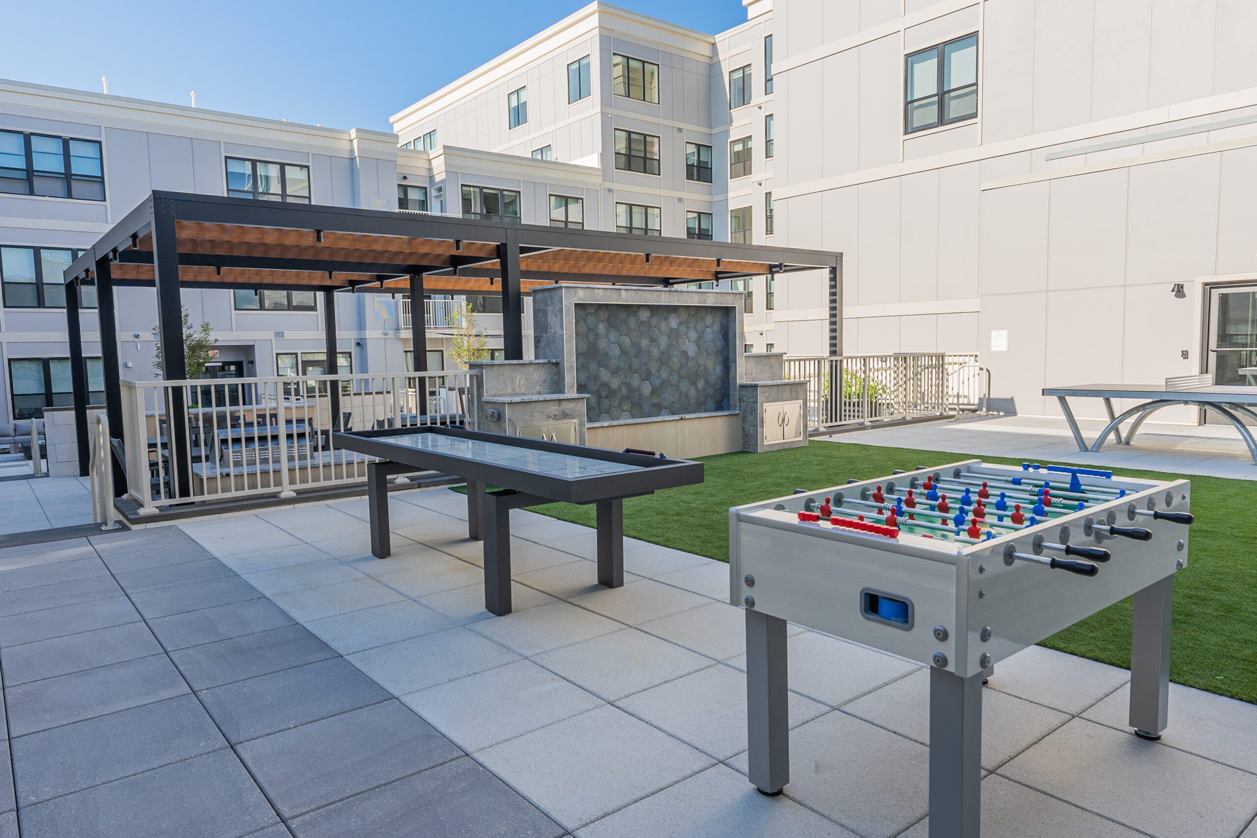 Modern urban courtyard featuring stylish pergola, foosball and shuffleboard tables, perfect for relaxation and entertainment.