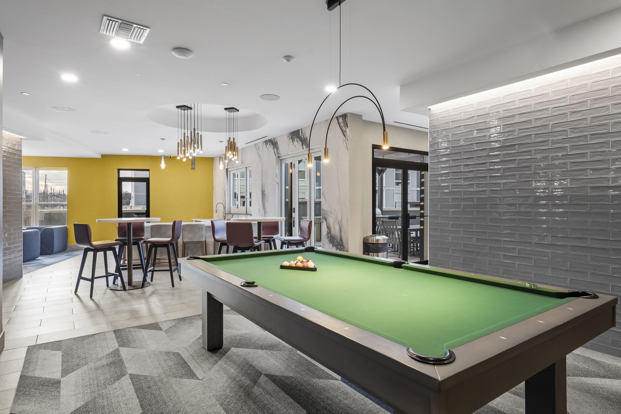 Modern and inviting communal lounge with a sleek pool table, vibrant yellow accent wall, and stylish seating area.