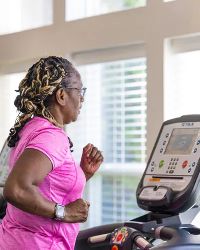 Energetic individual running on a treadmill in a bright, modern gym with large windows.