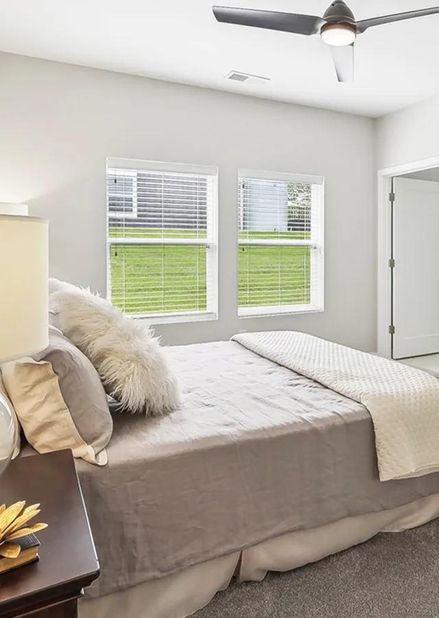 Bright and inviting bedroom with large windows offering garden views, modern ceiling fan, and cozy bedding for ultimate comfort.