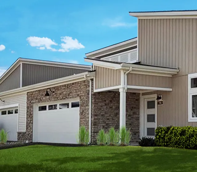 Modern home exterior with elegant stone facade, spacious garage, and lush green lawn under a clear blue sky.
