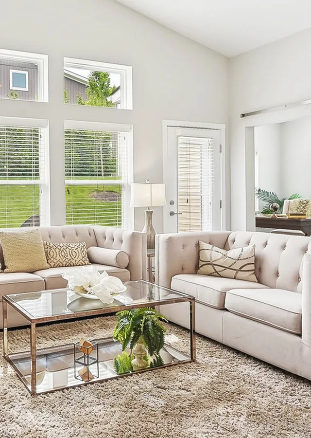 Bright and elegant living room with plush beige sofas, a glass coffee table, and large windows offering plenty of natural light.